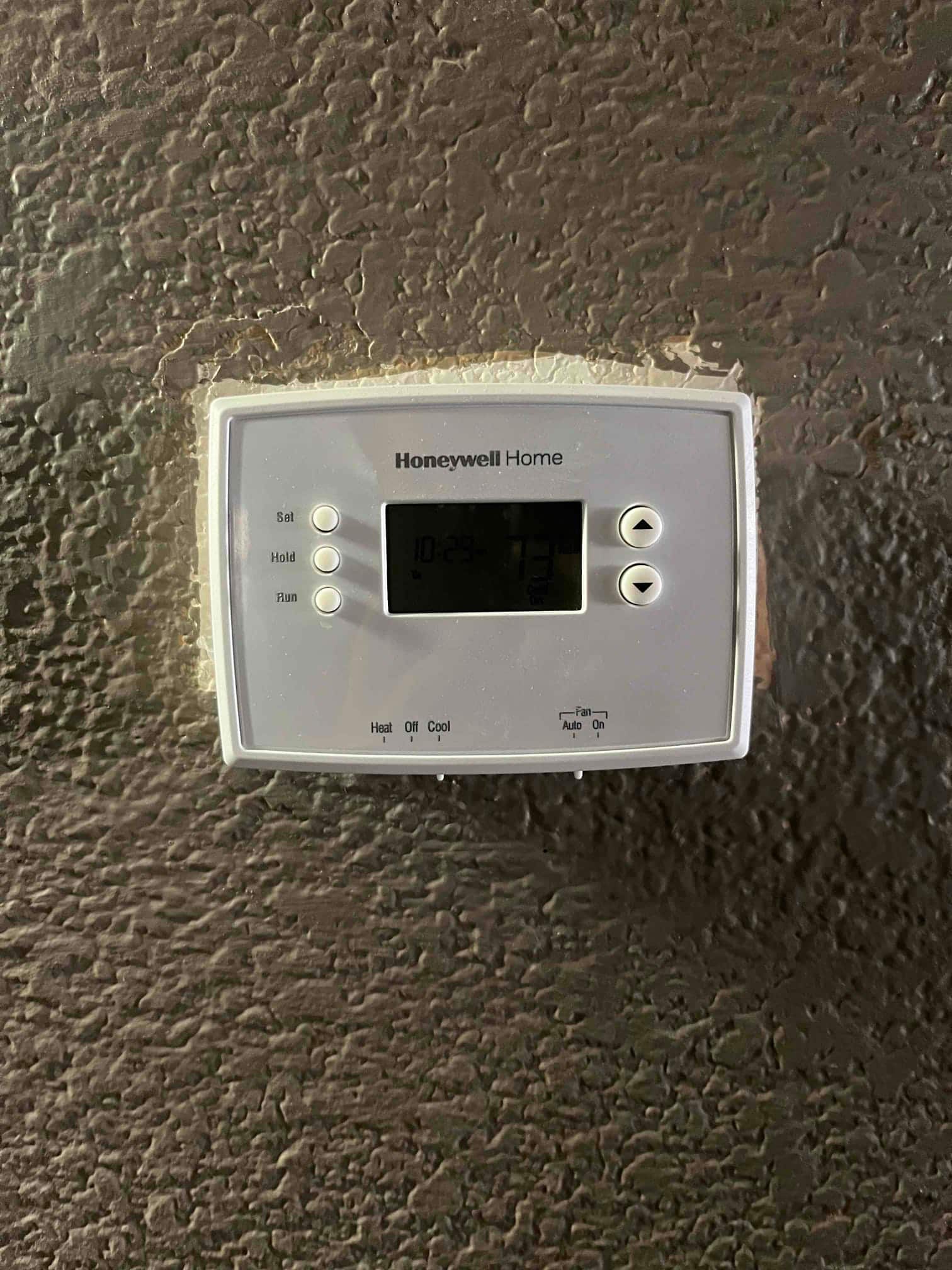 Wall-mounted thermostat with display illuminated and control buttons visible, set to Cool mode with fan set to Auto.