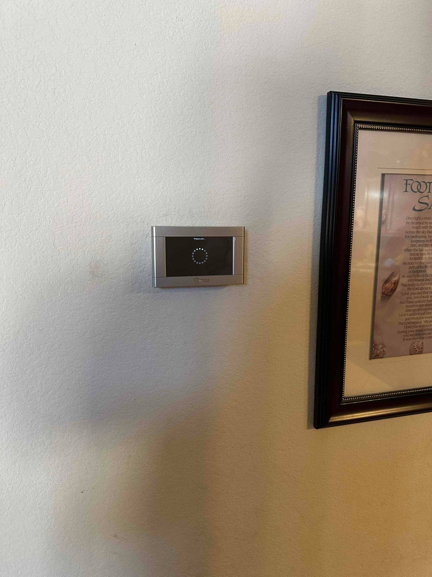 Wall-mounted thermostat installed and powering up, displaying a startup loading indicator on the screen beside a framed picture.