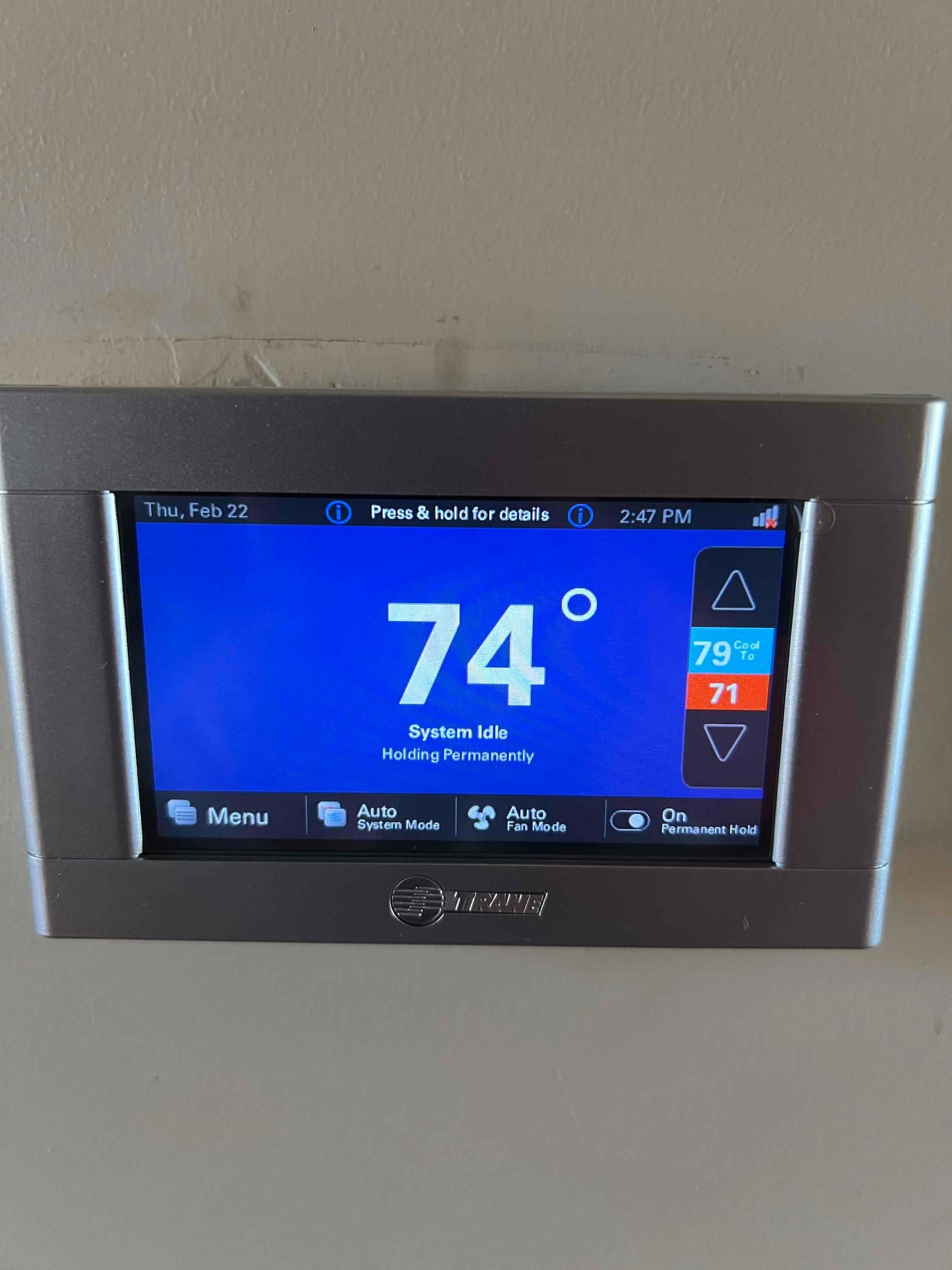 Wall-mounted touchscreen thermostat displays 74 degrees with system idle status and controls for system and fan modes.