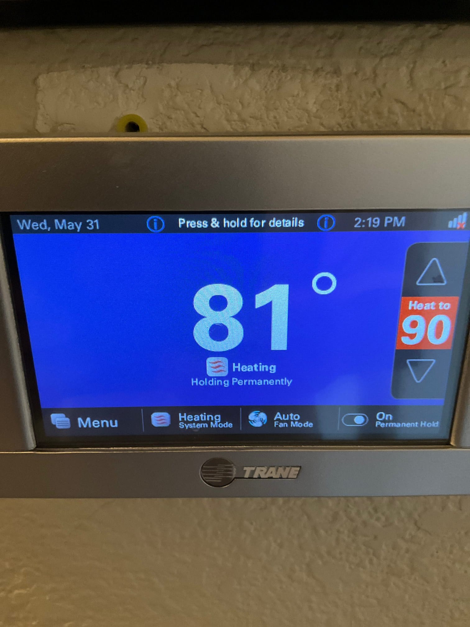 Wall-mounted touchscreen thermostat displays 81 degrees with system set to heating mode on permanent hold.