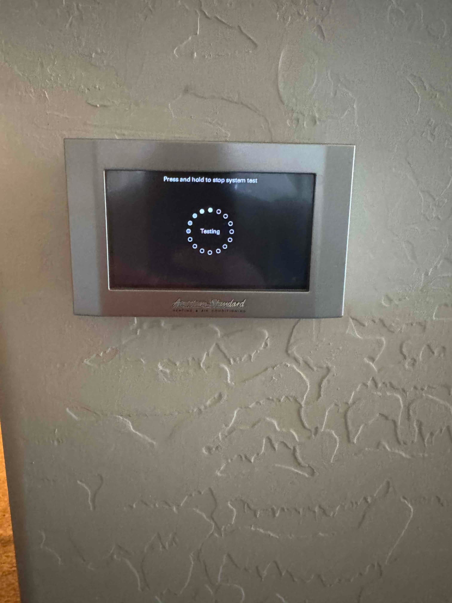 Wall-mounted touchscreen thermostat displays a system test screen during post-installation checkout of the HVAC controls.