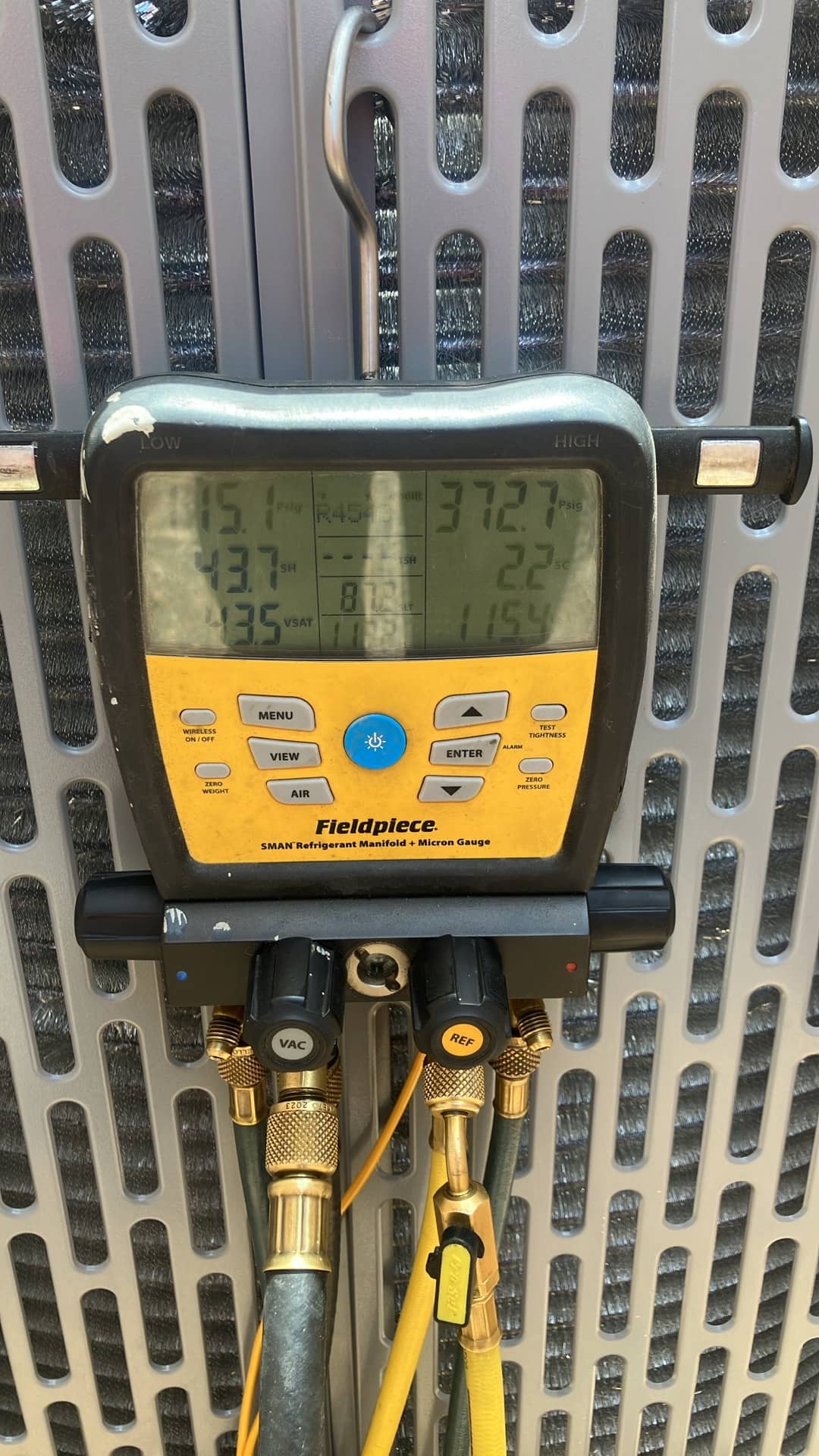 Digital manifold shows system operating pressures with hoses connected at the outdoor unit during commissioning.
