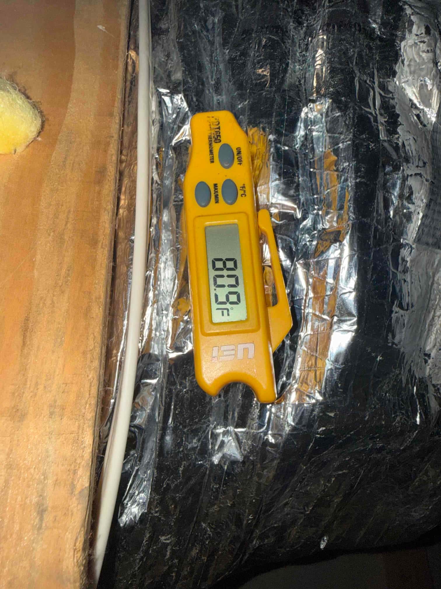 Digital thermometer reads 80.0°F while checking air temperature at ductwork during HVAC commissioning.