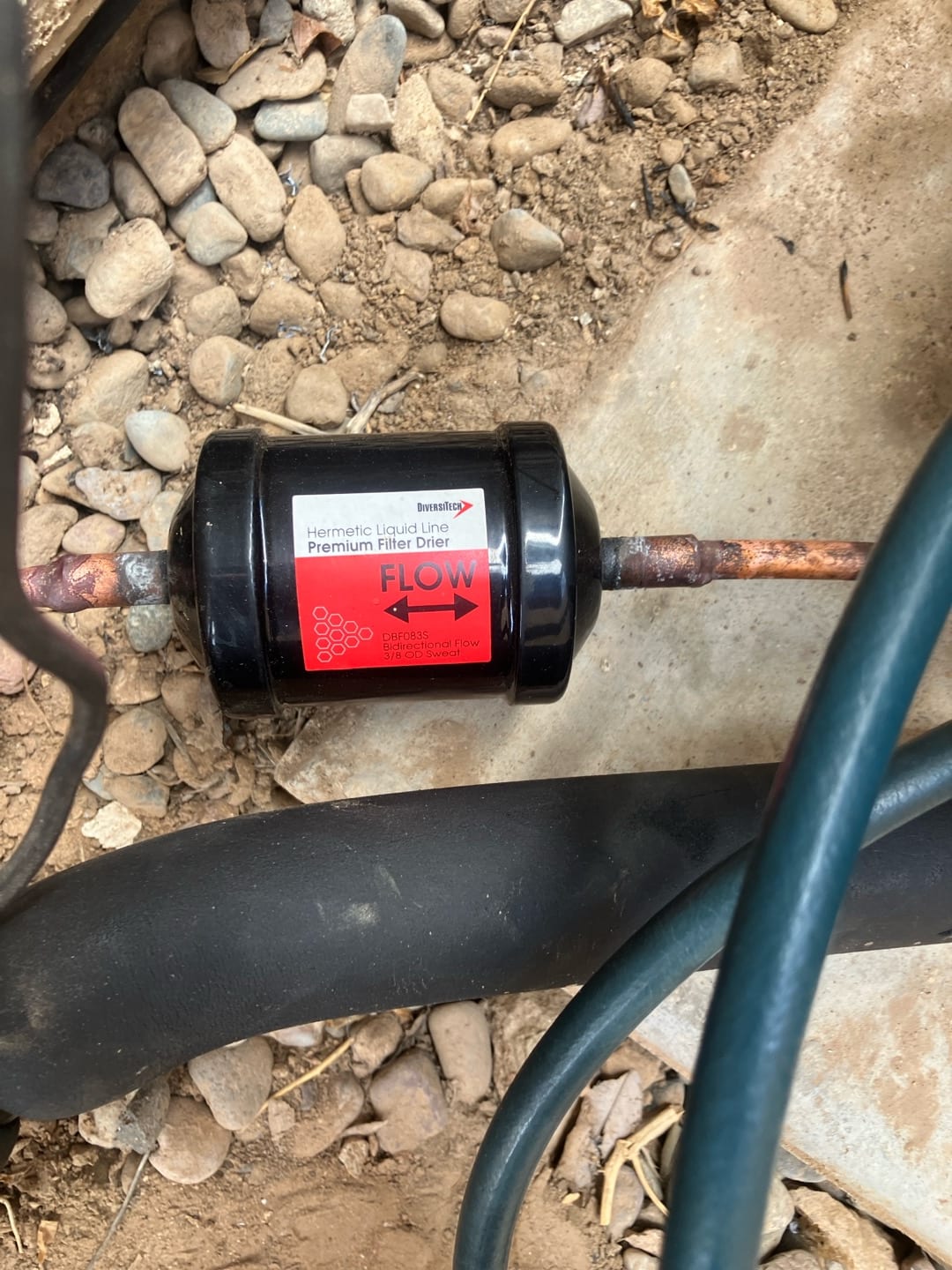 Hermetic liquid-line filter drier brazed into the copper line set, with flow direction indicated by the arrow on the label.