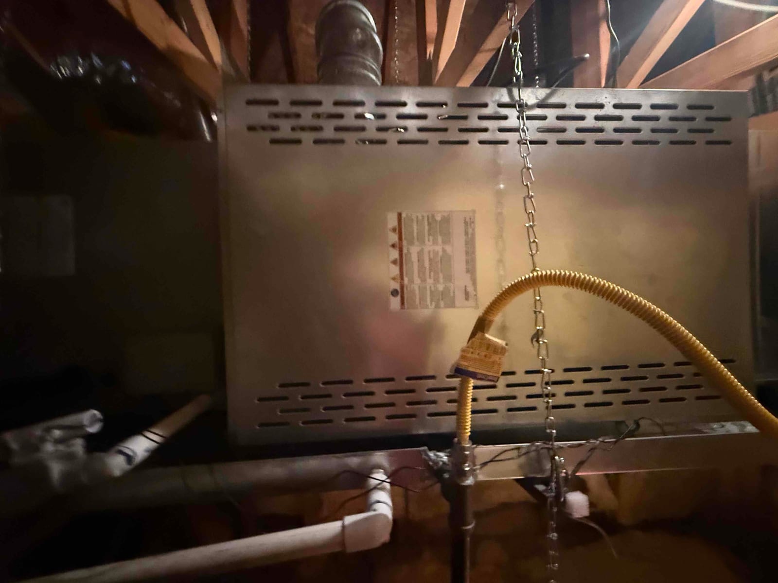 Horizontal gas furnace or air handler suspended in the attic with venting, gas flex connector, and condensate drain piping visible.