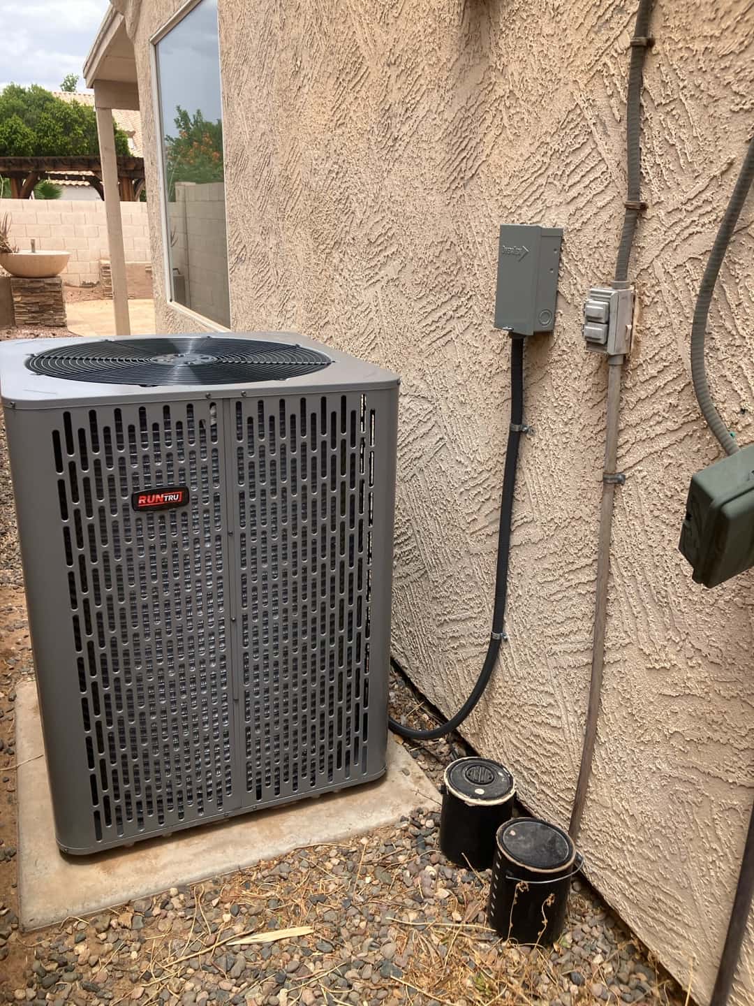 New outdoor condenser set on a level pad with electrical disconnect mounted and refrigerant line set routed into the wall.