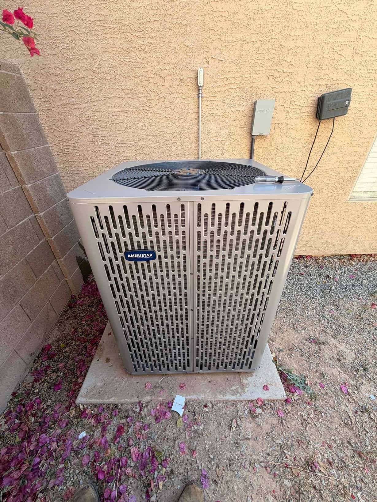 New outdoor condenser set on a level pad with electrical whip and disconnect mounted on the wall nearby.