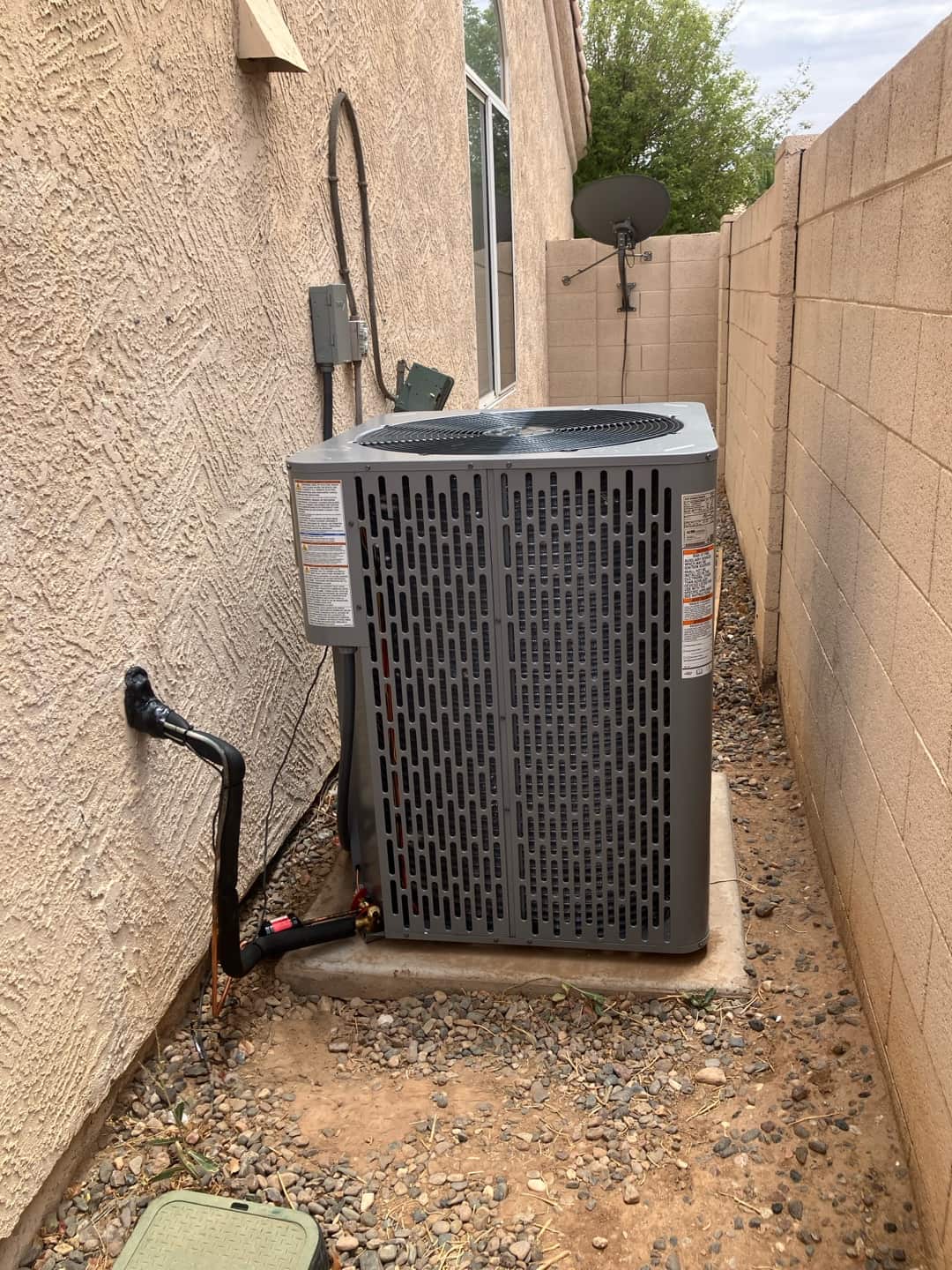 New outdoor condenser set on a level pad with insulated refrigerant lines, sealed wall penetration, and electrical disconnect mounted nearby.