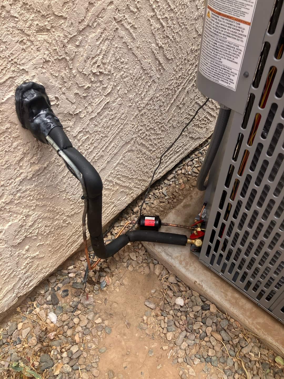 Refrigerant line set enters the wall with sealed penetration and insulated suction line beside the new outdoor condenser on a level pad.