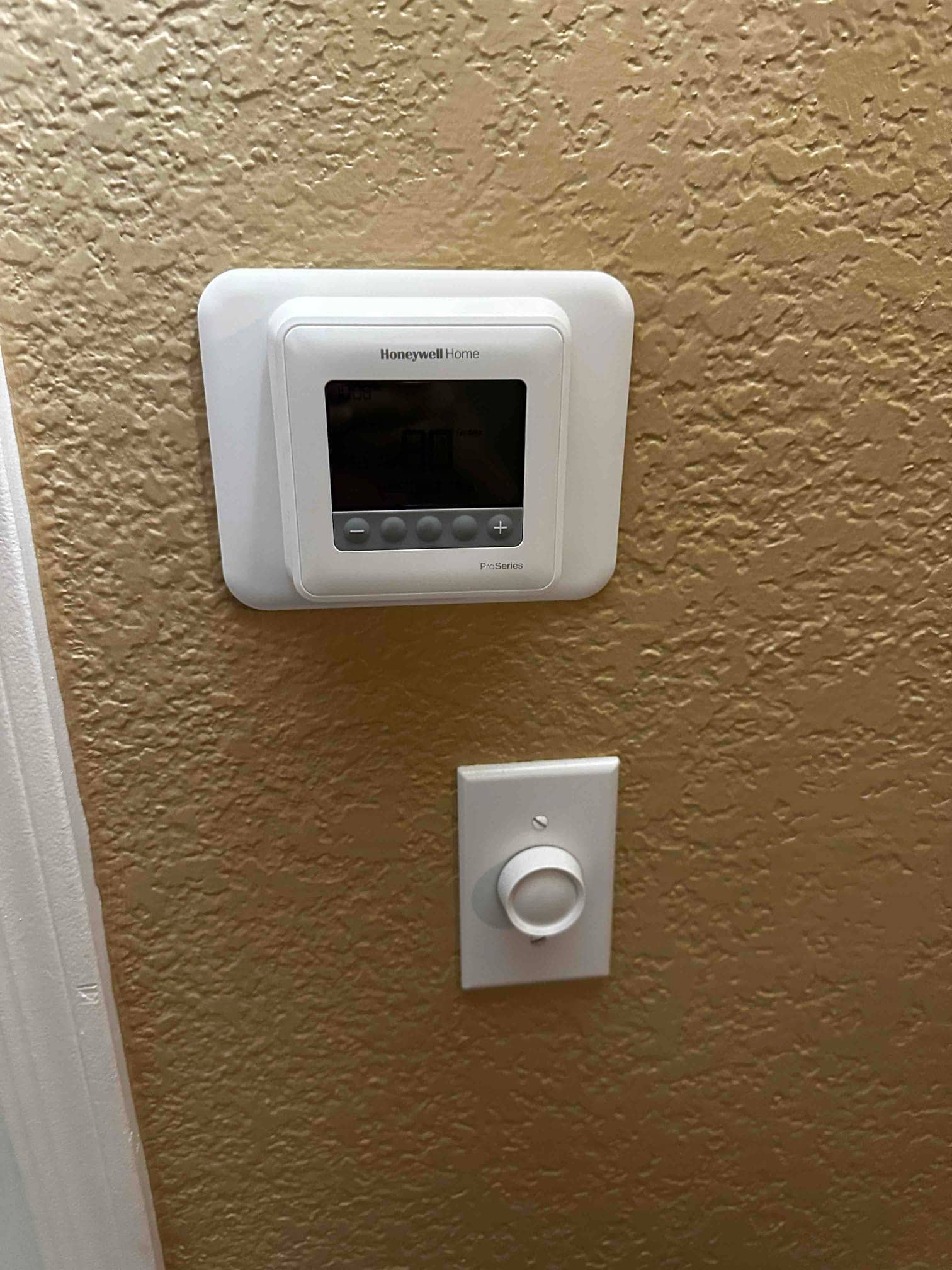 Wall-mounted thermostat with adjacent control knob installed on finished interior wall, showing completed controls for the new HVAC system.