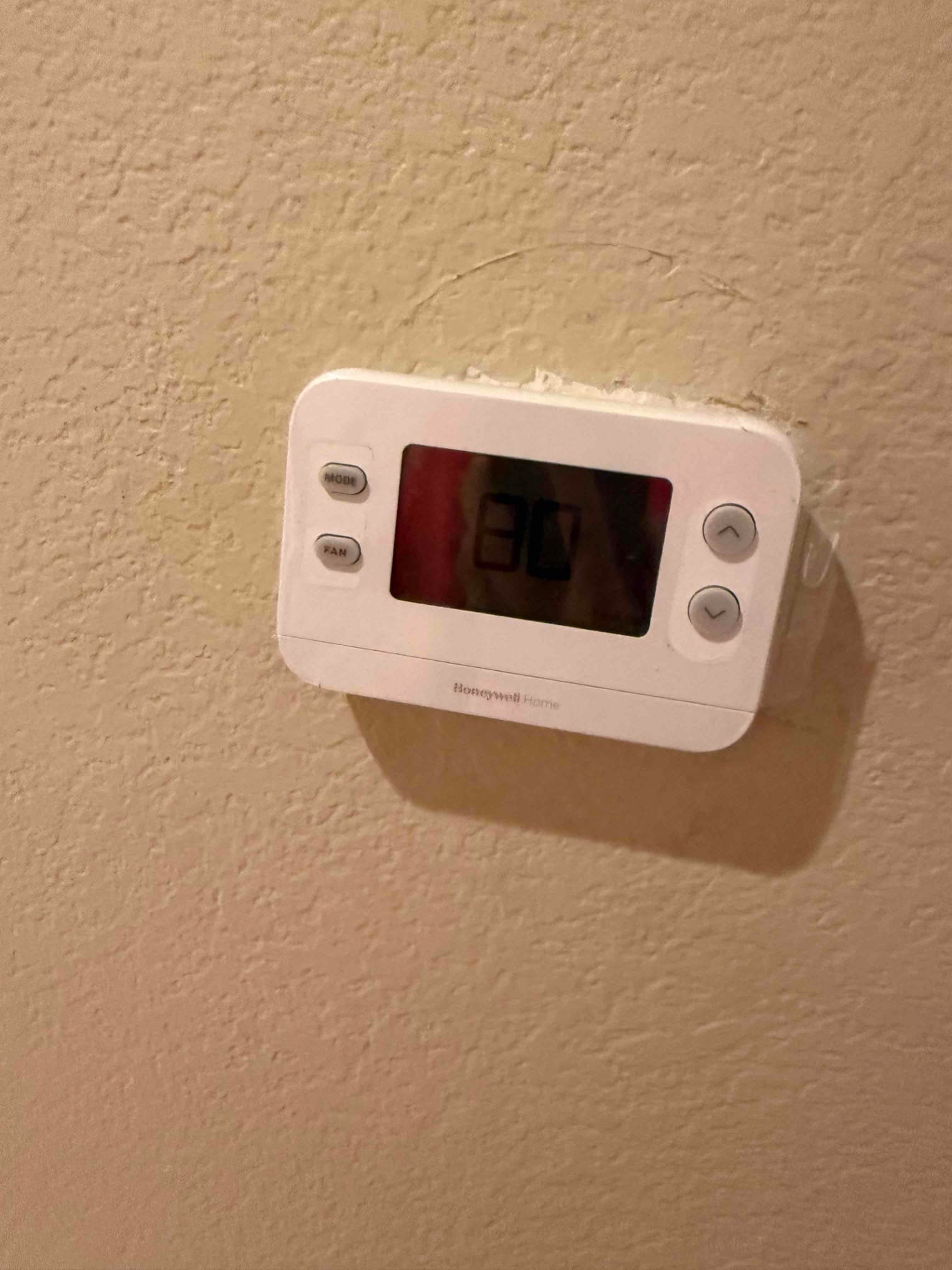 Wall-mounted thermostat installed and powered on, displaying room temperature on its digital screen with control buttons visible.