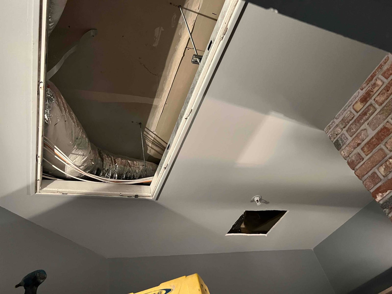 Attic access open with new insulated flex duct and control wiring routed above the ceiling during installation work.