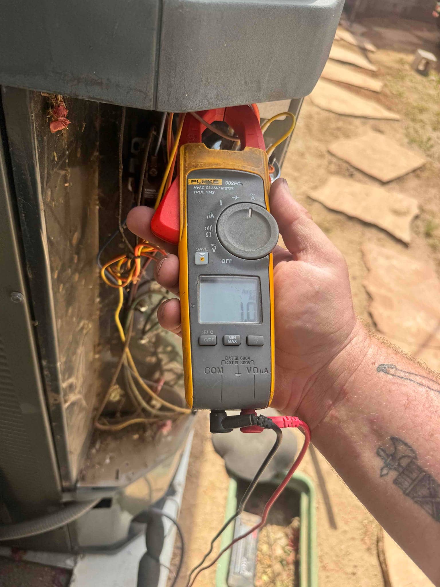 Clamp meter displays 1.0 A with the jaw clamped on a conductor at the outdoor condenser.