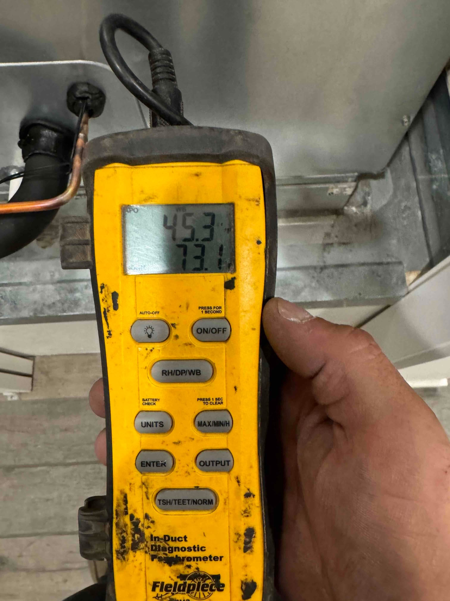 Digital in-duct thermometer probe inserted into metal duct, display showing 45.3 and 73.1 degrees during airflow temperature checks.