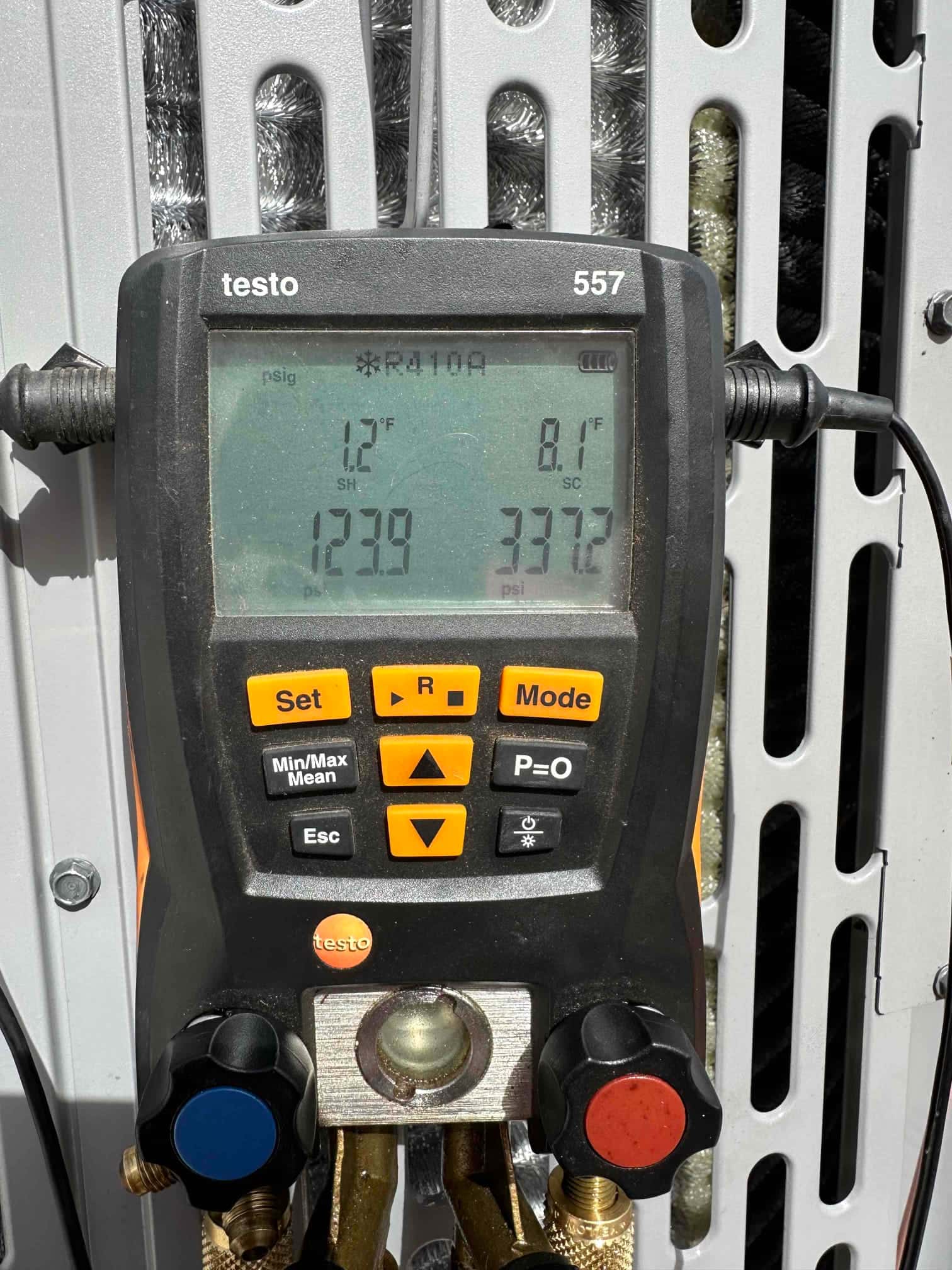 Digital manifold connected to the condenser shows operating pressures and calculated superheat and subcooling during system commissioning.