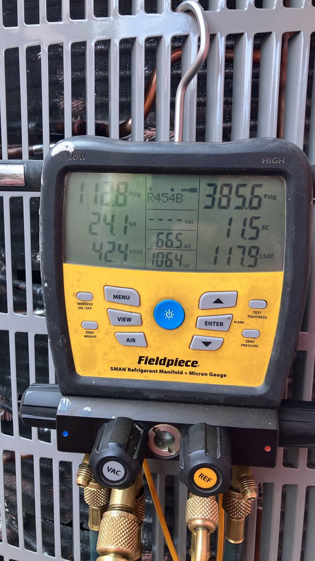 Digital manifold shows system operating pressures and calculated values during commissioning on an outdoor condenser.