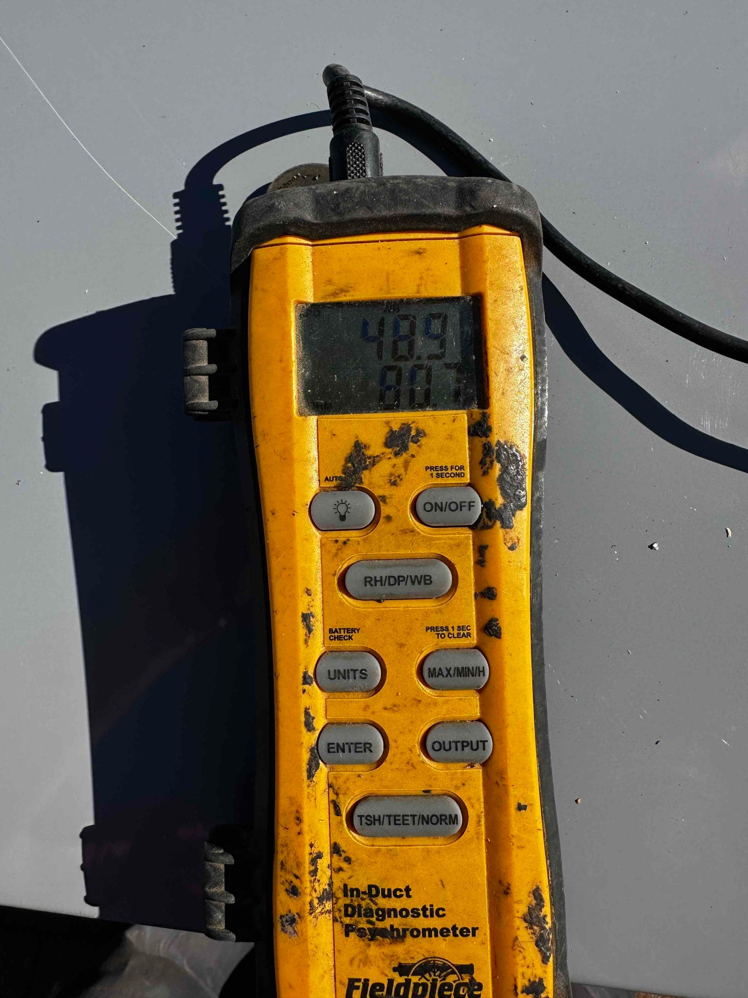 Digital psychrometer displays 48.9 degrees Fahrenheit, documenting supply air temperature during system checkout.