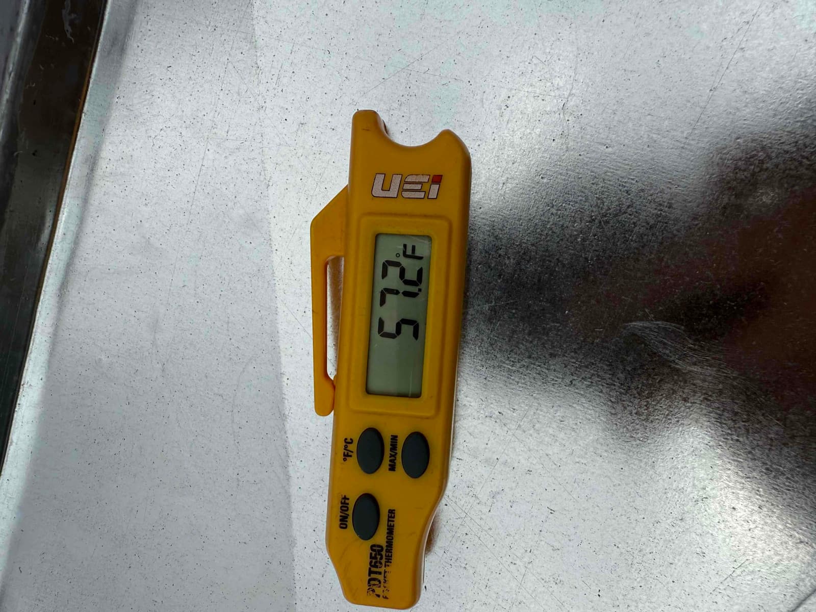 Digital thermometer displays 57.2°F, documenting cool supply air temperature at the metal duct surface.