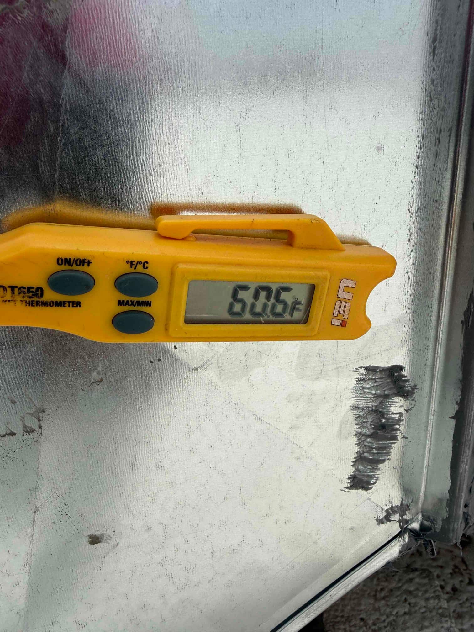 Digital thermometer on metal duct shows 60.6°F, documenting supply air temperature at the outlet during commissioning.