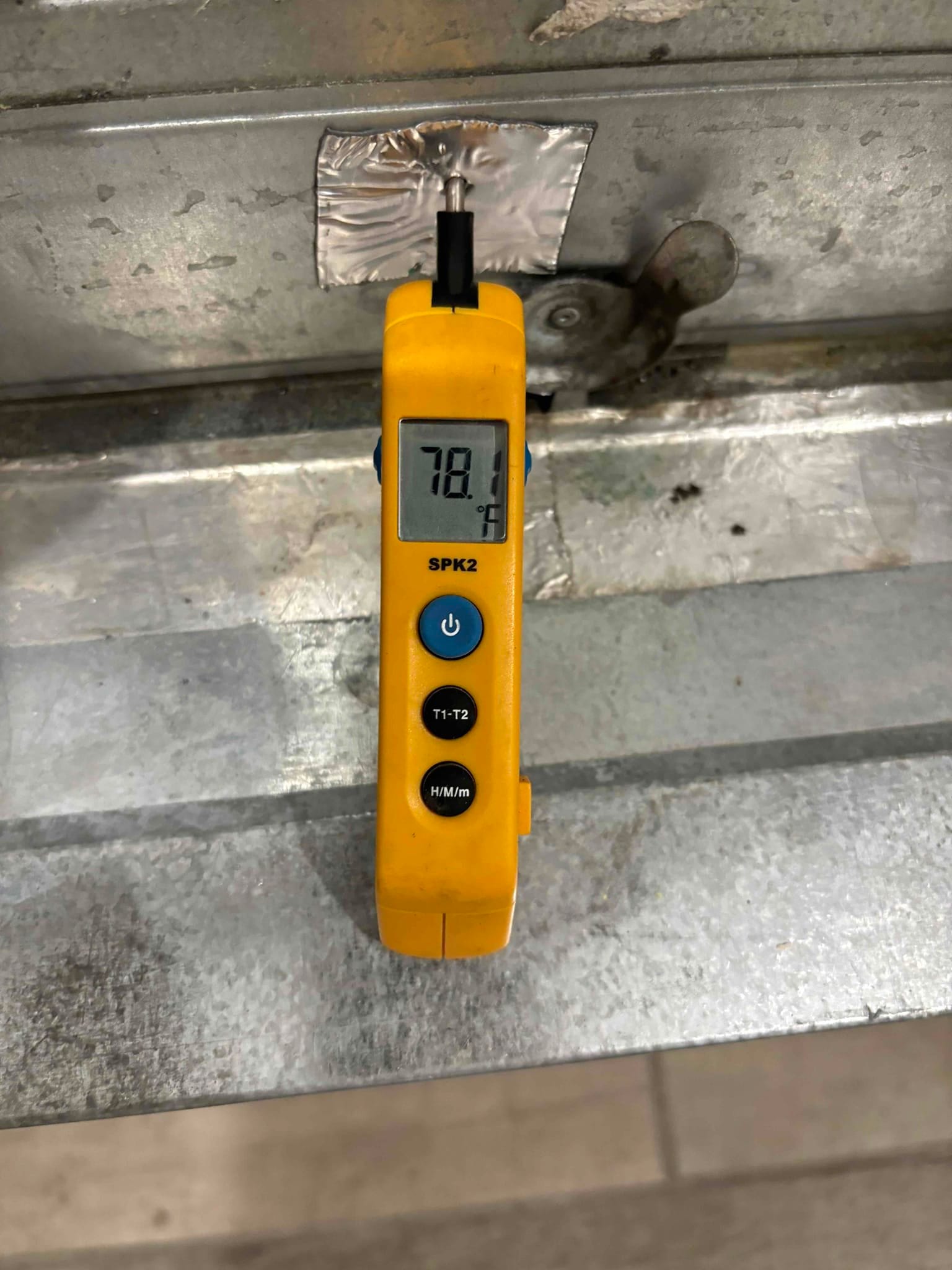 Digital thermometer probe contacts a metal duct surface, displaying 78.1 degrees Fahrenheit during return air temperature check.