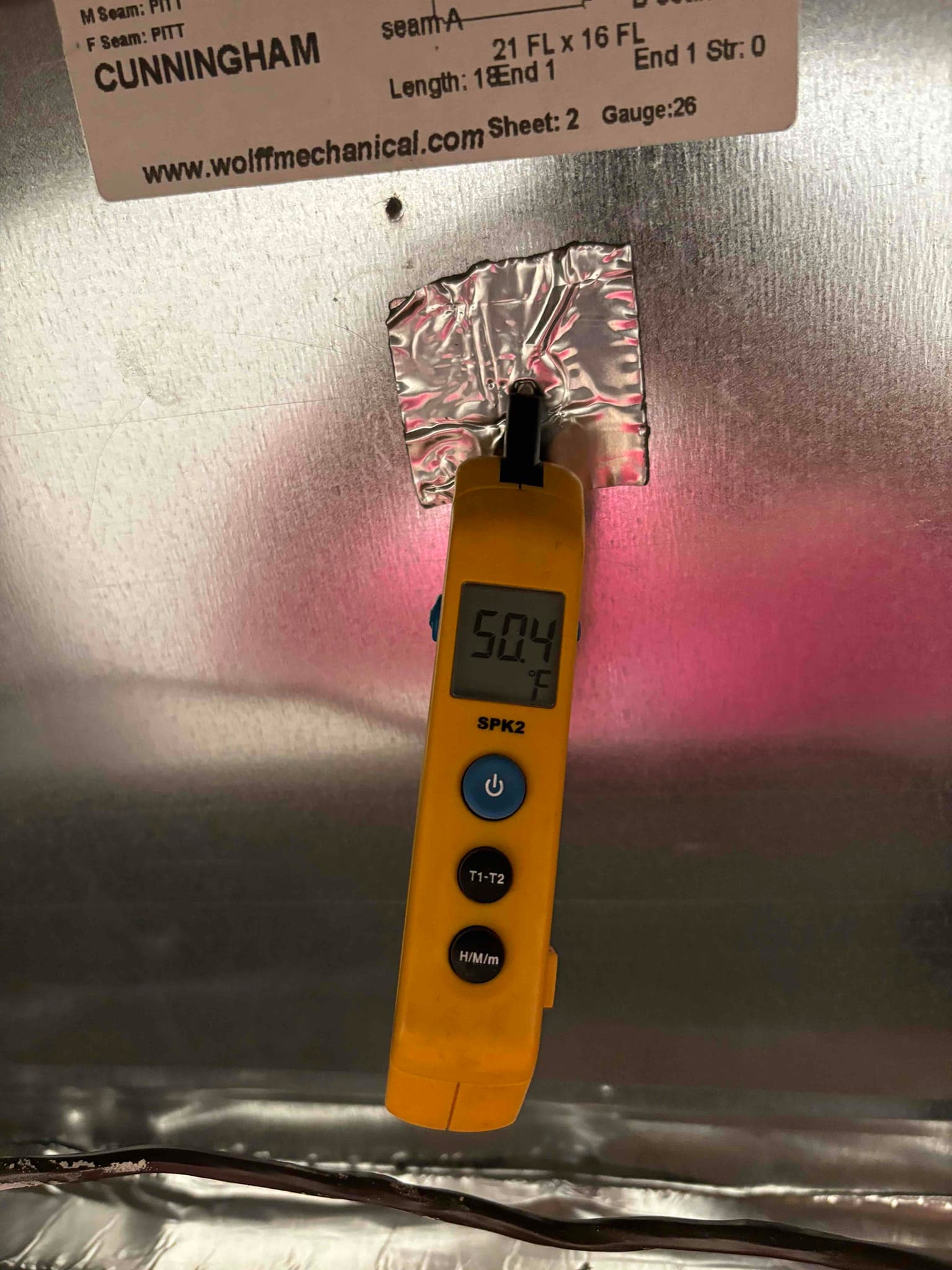 Digital thermometer probe inserted into duct measures supply air at 50.4°F, documenting cooling performance after installation.