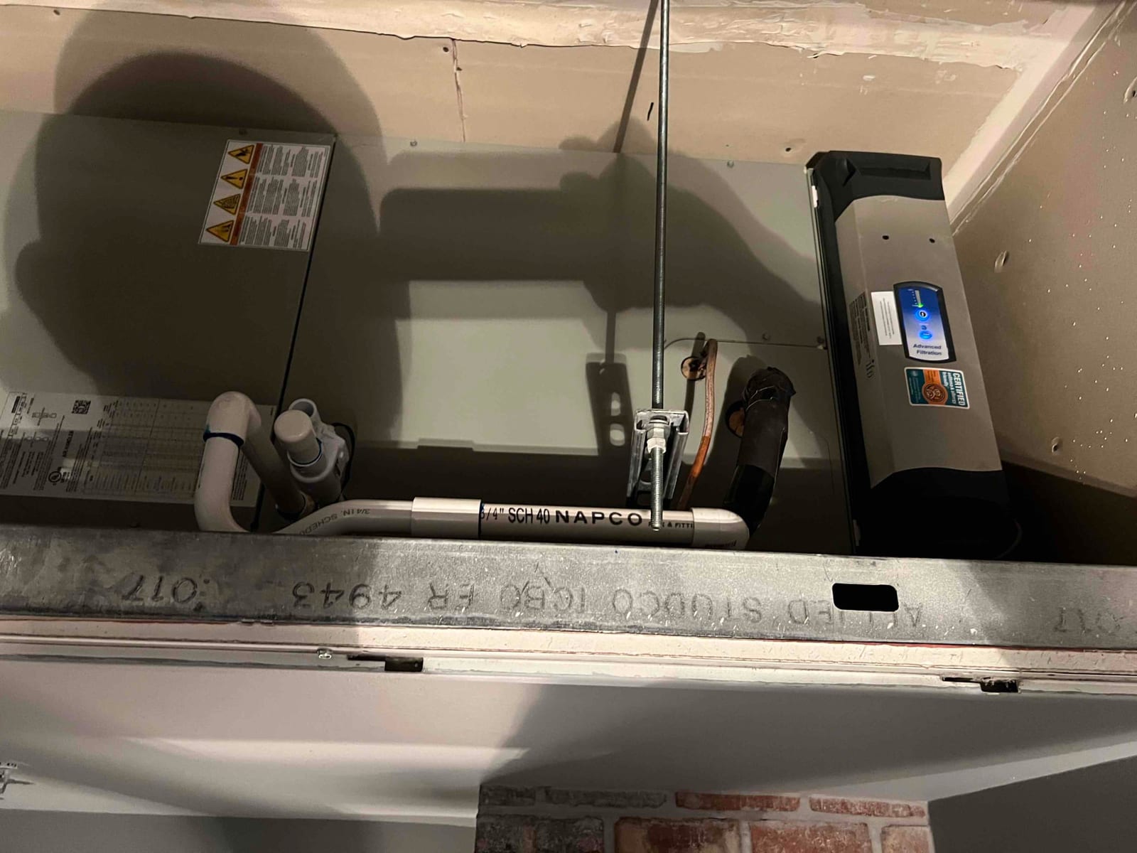 Indoor air handler installed with condensate drain, insulated refrigerant lines, hanging support rods, and an in-duct air purifier powered on.