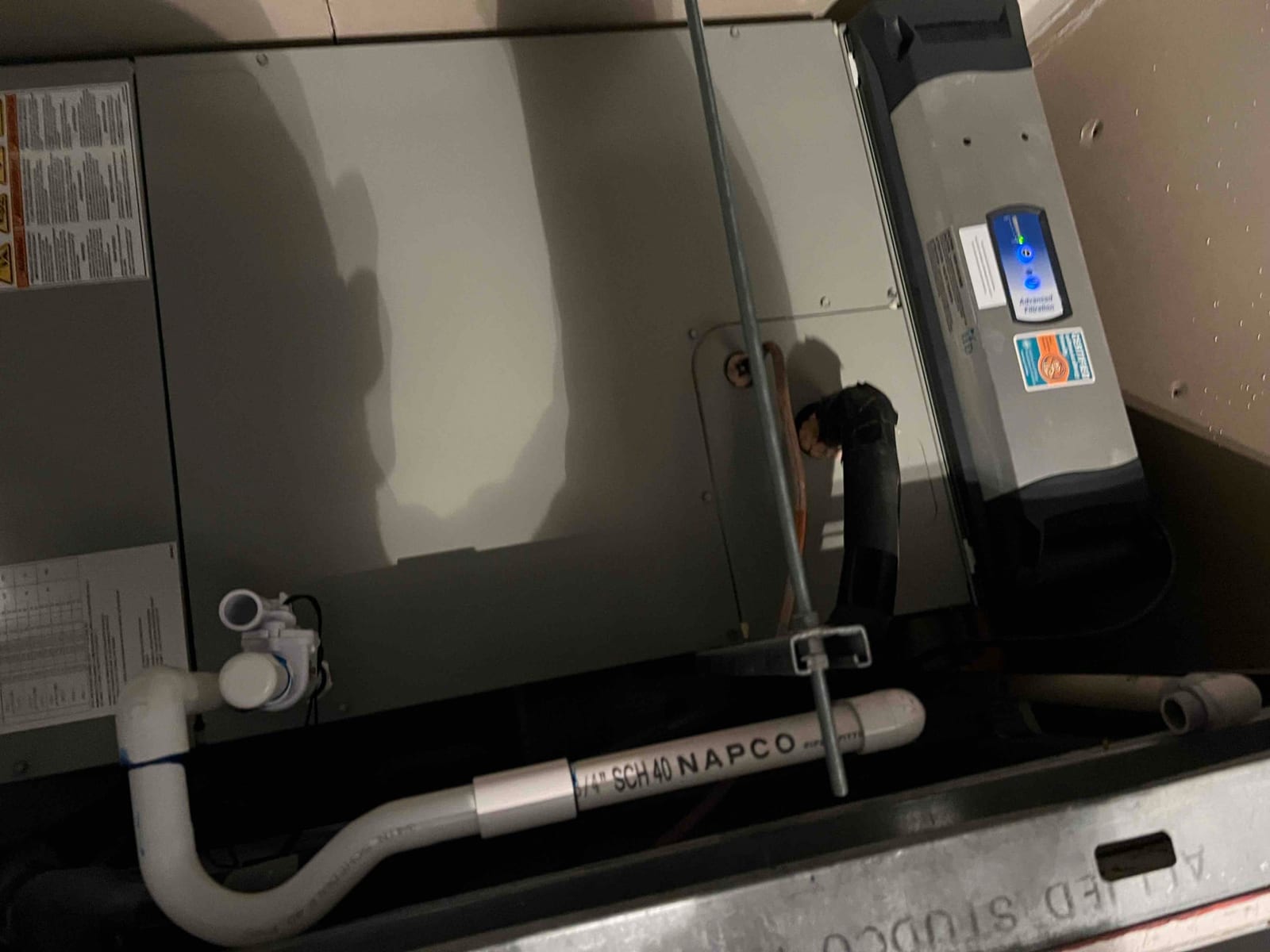 Indoor air handler installed with condensate drain piping, insulated refrigerant line, and an inline air purification device energized.