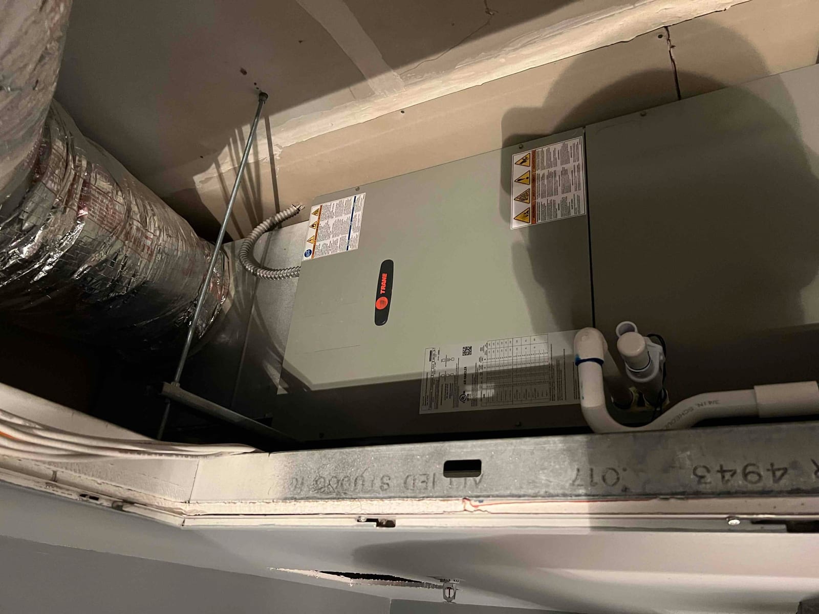New air handler installed in ceiling space with insulated duct connection, electrical whip, and condensate drain piping tied into the trap.