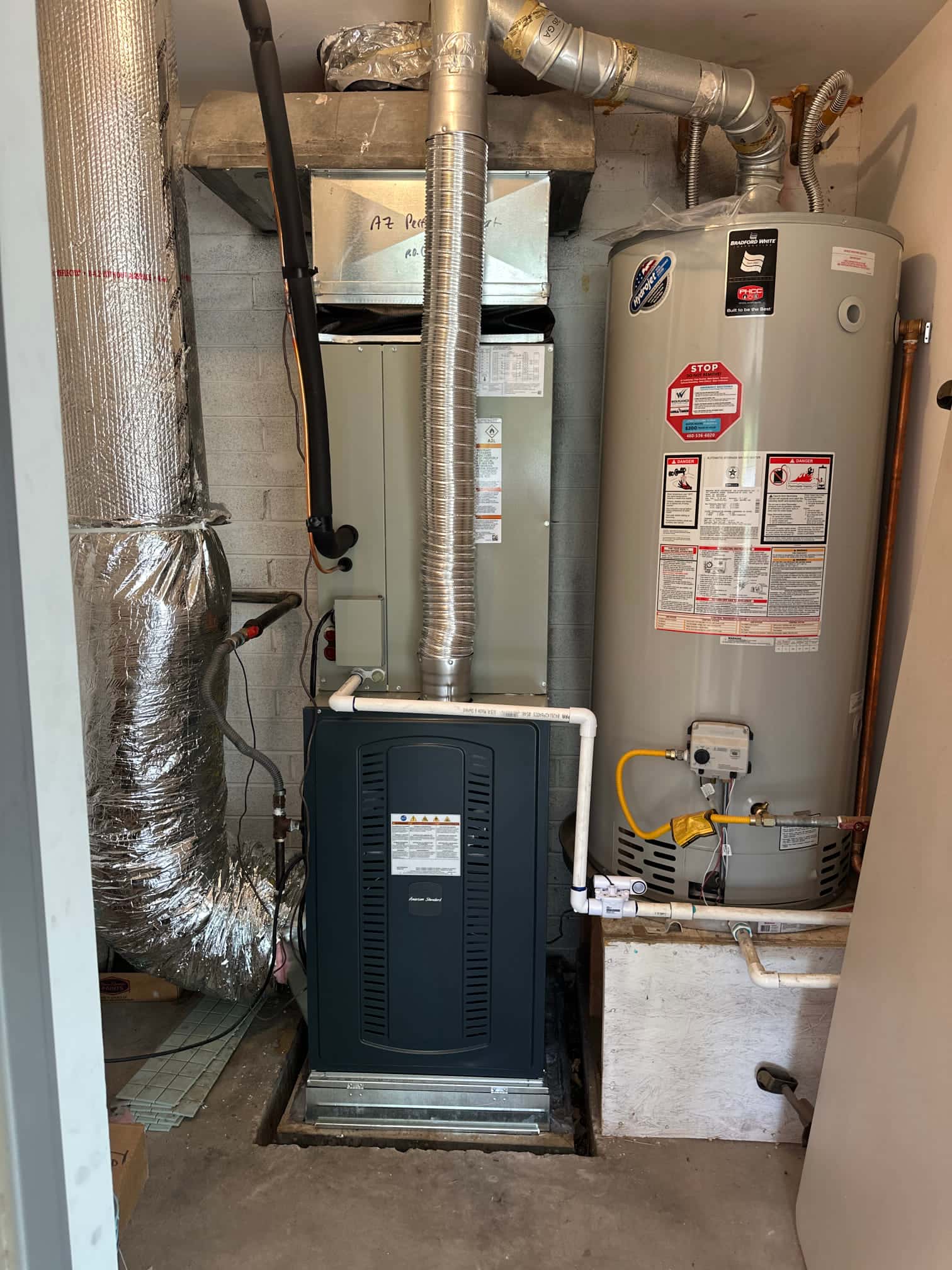 New furnace and evaporator coil installed with flue venting, insulated refrigerant line, condensate drain, and adjacent water heater in utility closet.