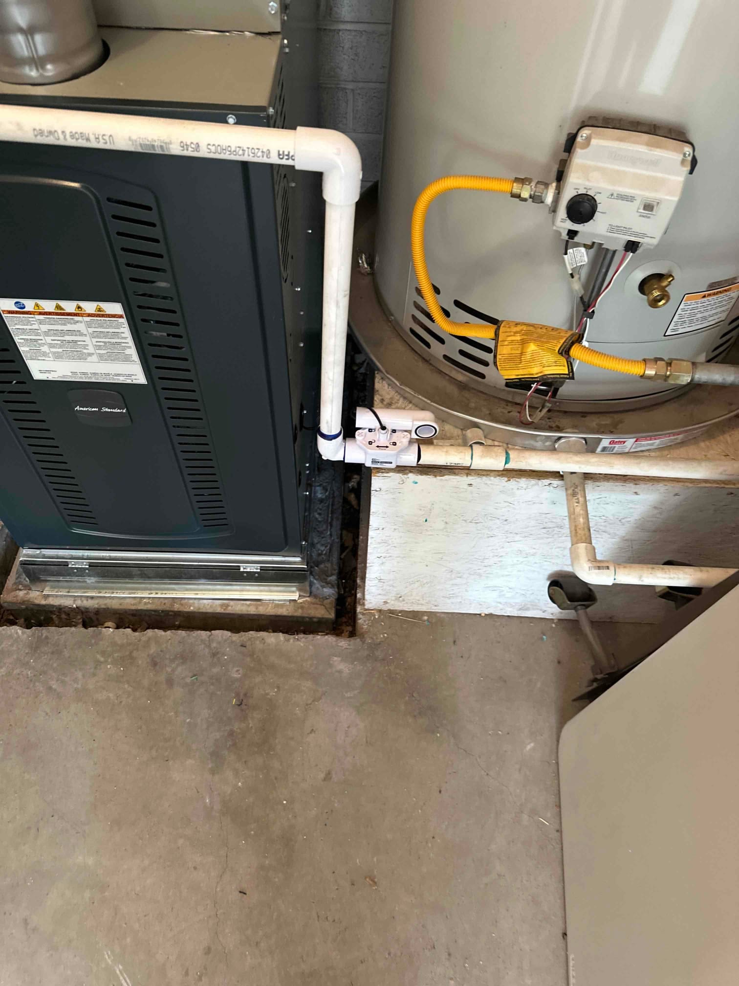 New furnace set in place with PVC condensate drain piping routed beside an adjacent water heater and gas line.