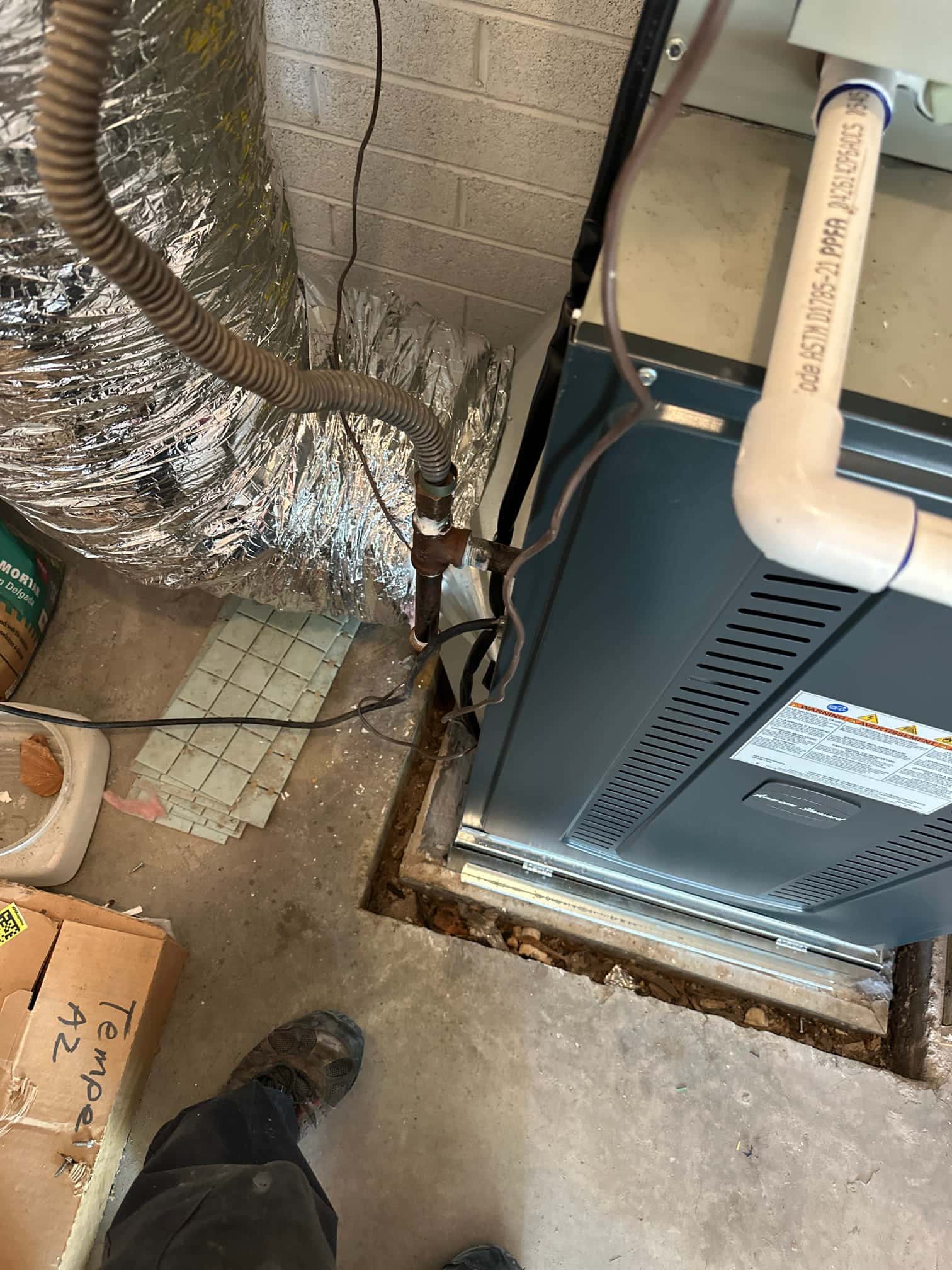 New gas furnace set in place with condensate drain piping and insulated duct connection visible at the installation site.
