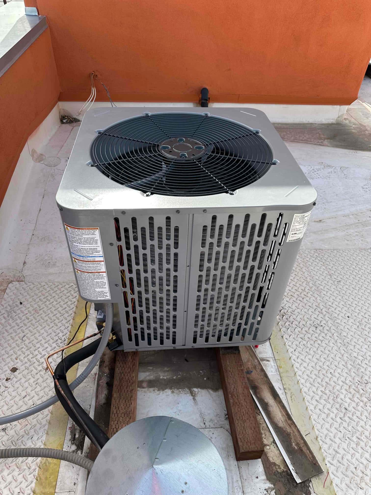 New outdoor heat pump condenser set on rooftop sleepers with insulated refrigerant lines and electrical whip routed to the unit.