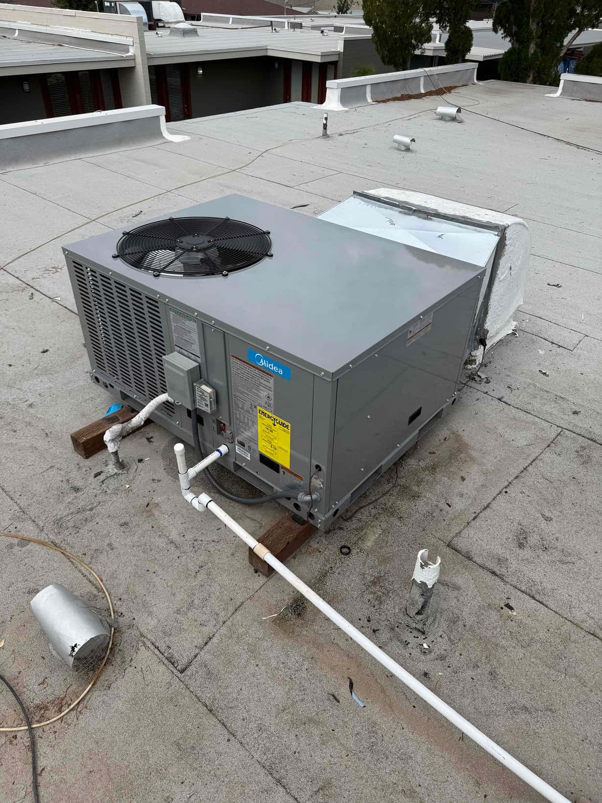 New rooftop package HVAC unit set on blocks with connected duct transition and condensate drain piping routed across the roof.