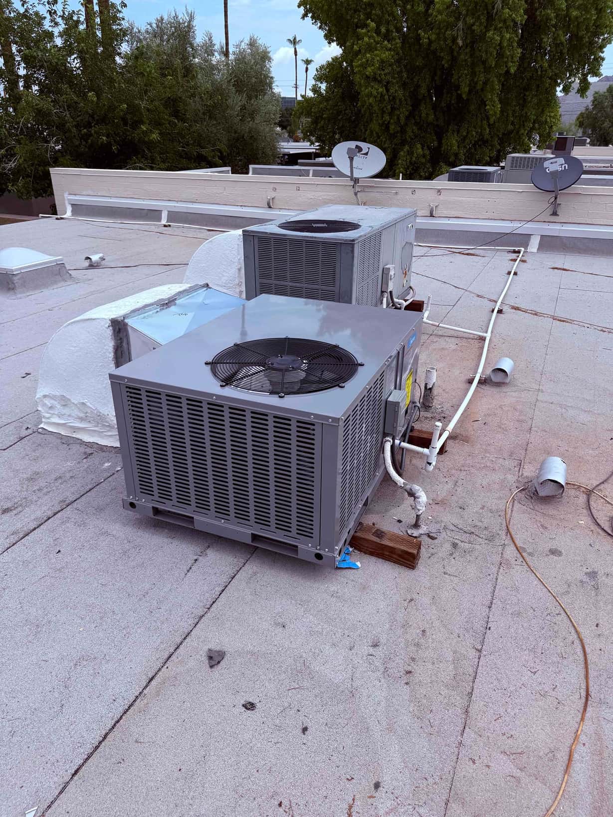 New rooftop package unit set on supports with connected refrigerant and condensate lines next to existing equipment and duct curb.