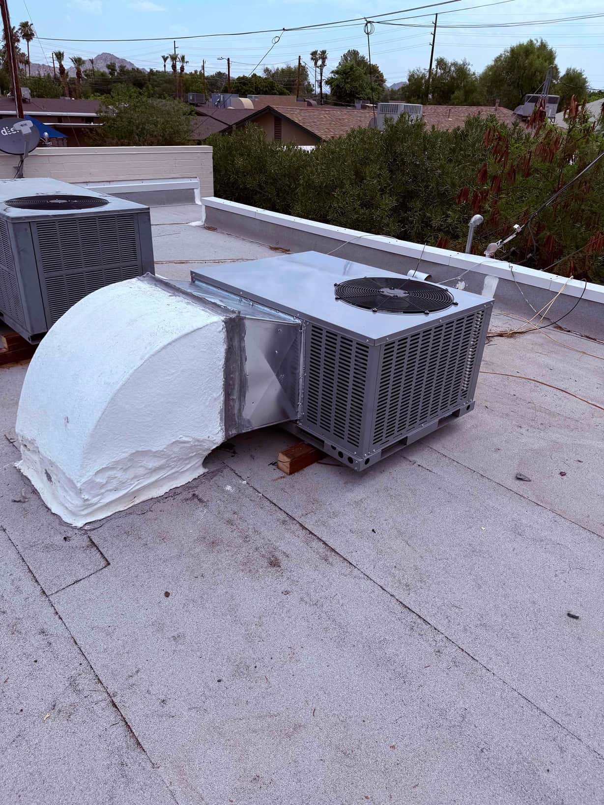 New rooftop package unit set on supports with sealed duct transition connected to the curb, next to an existing unit.
