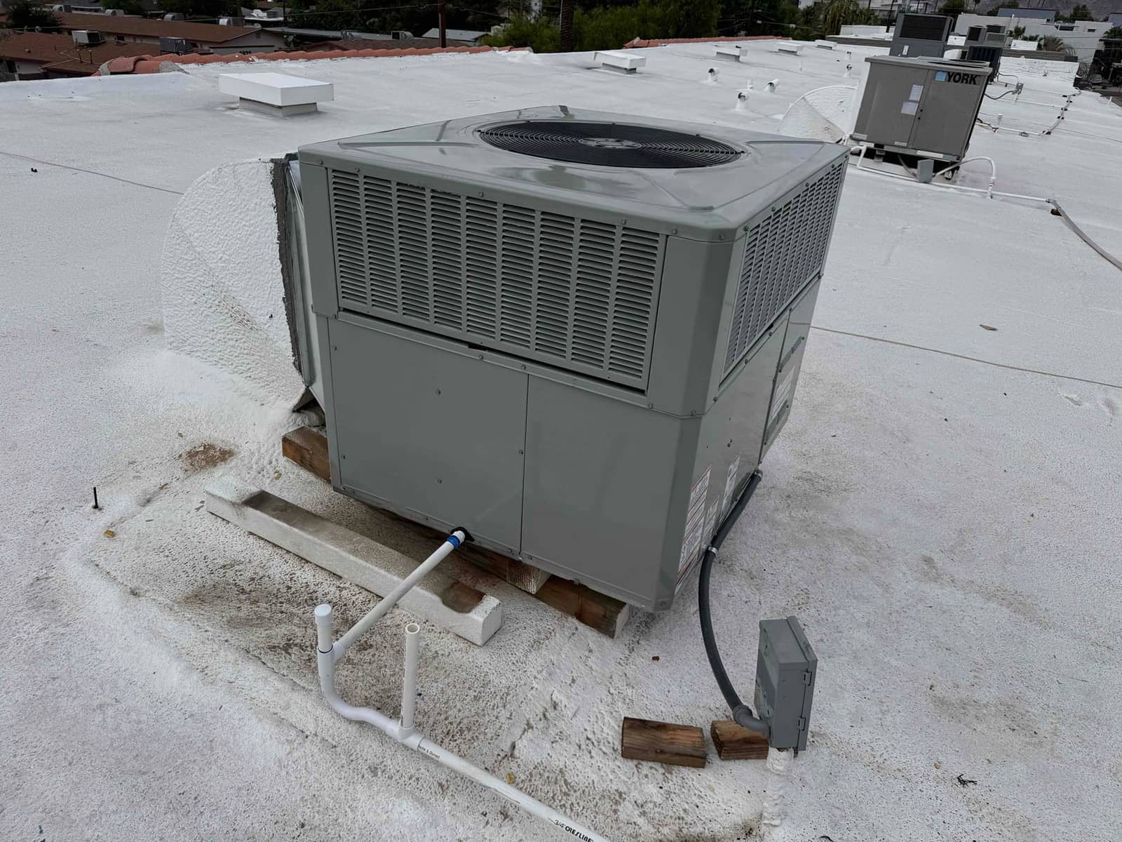 New rooftop packaged HVAC unit set on blocks with condensate drain piping and weatherproof electrical disconnect installed.