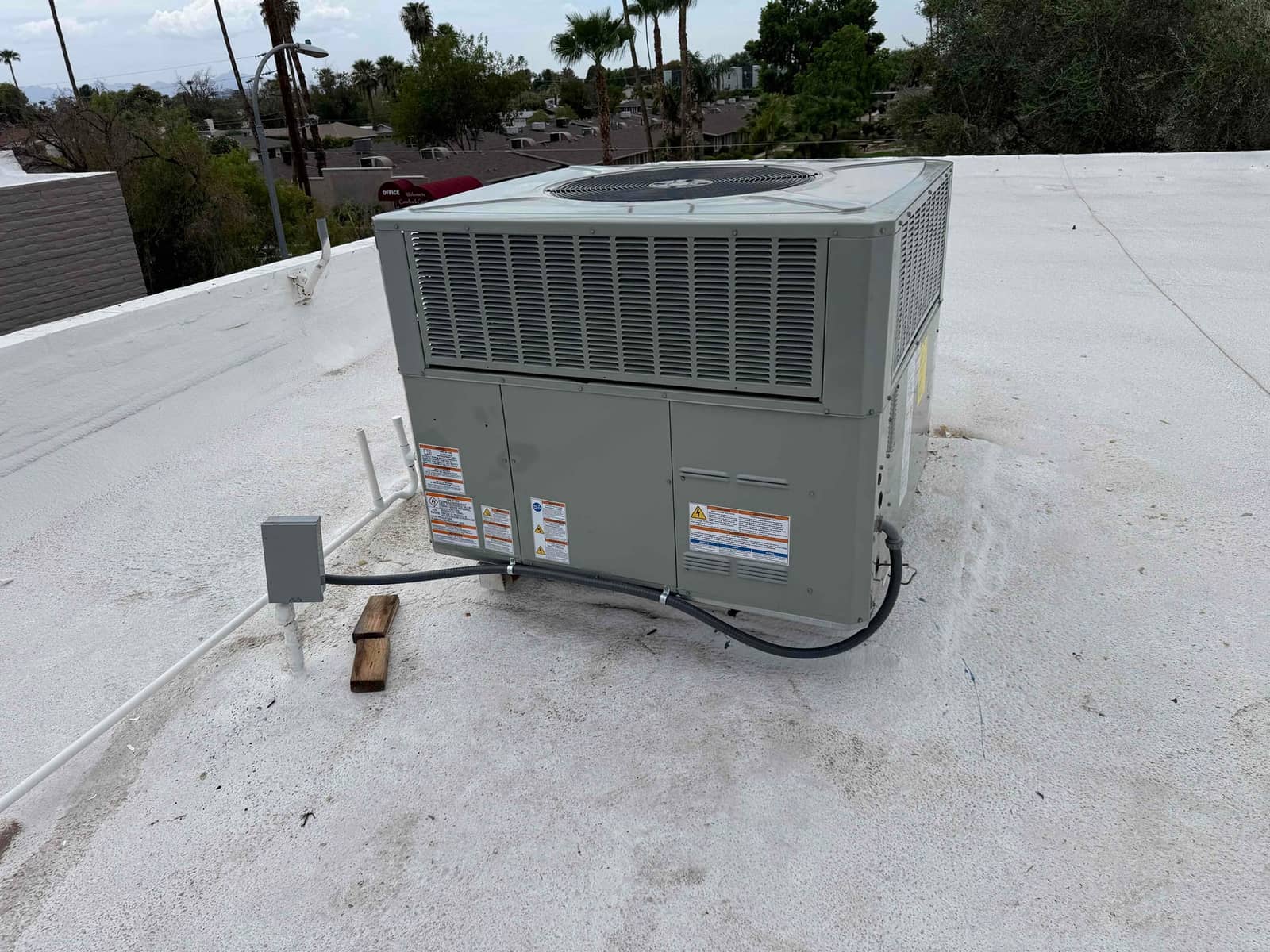 New rooftop packaged HVAC unit set on coated roof with weatherproof disconnect and flexible conduit connected.