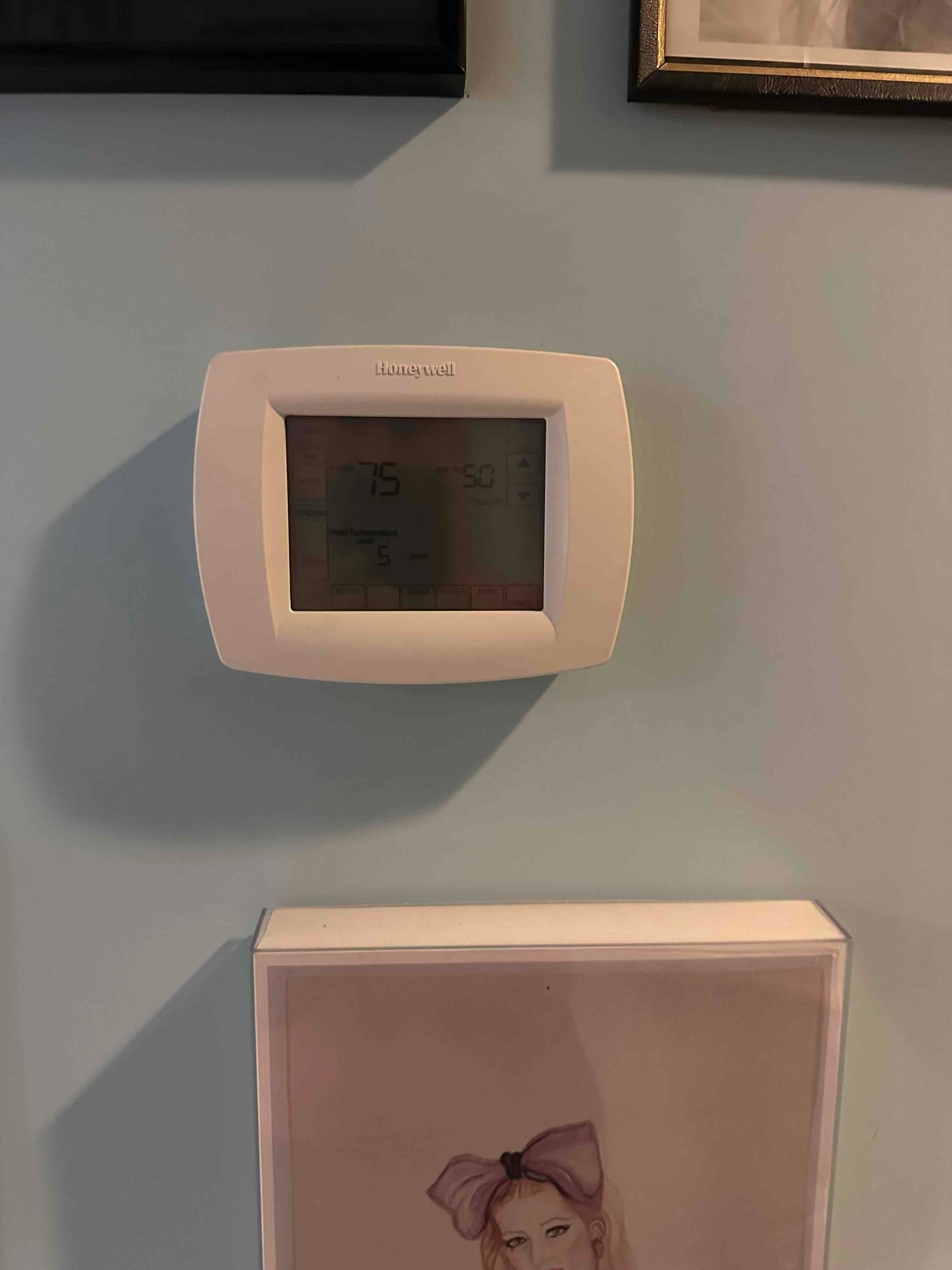 Wall-mounted digital thermostat installed and powered on, displaying room temperature and system status in a finished interior space.