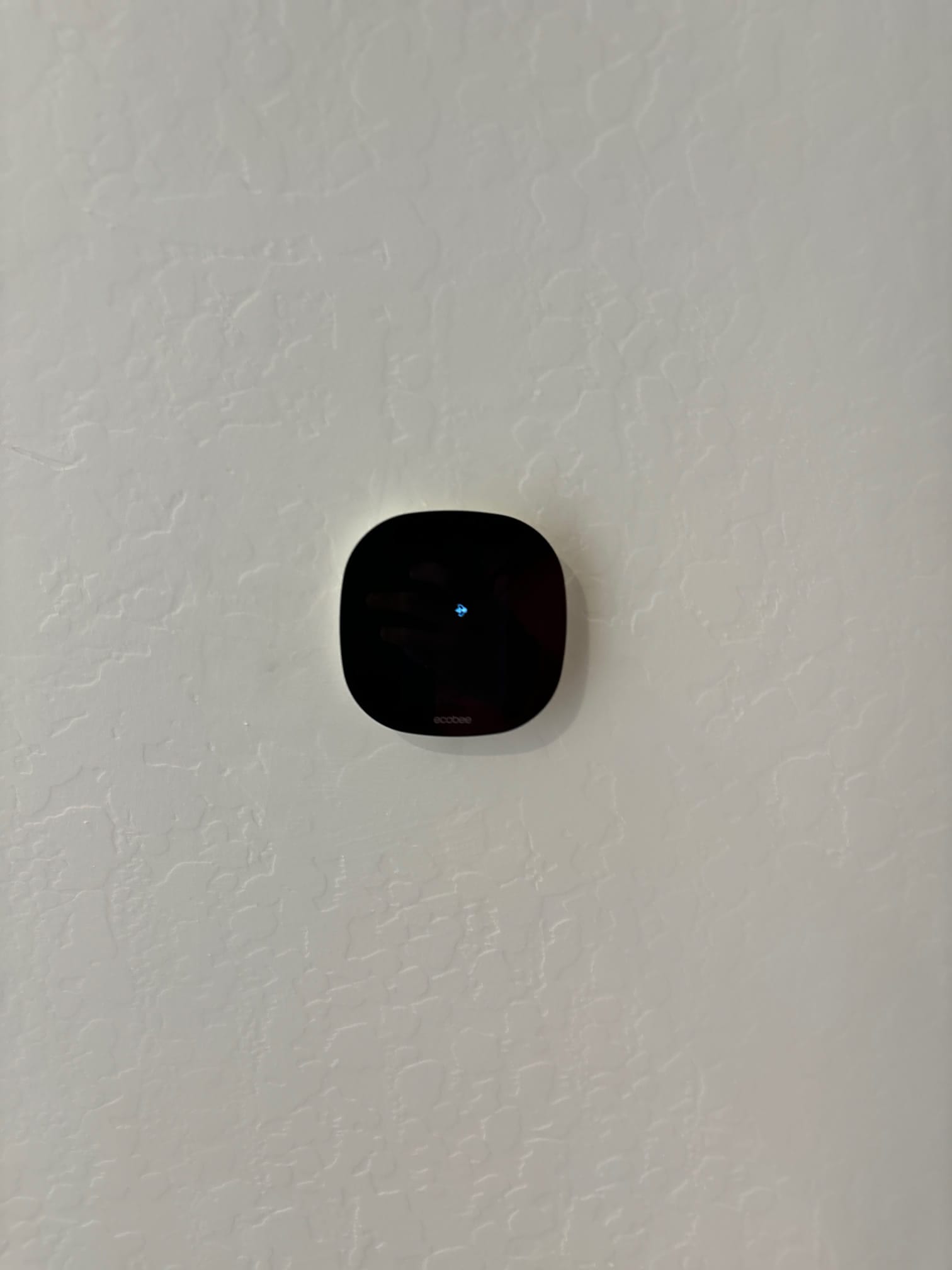 Wall-mounted smart thermostat installed and powered on, showing a single indicator light against a textured wall.