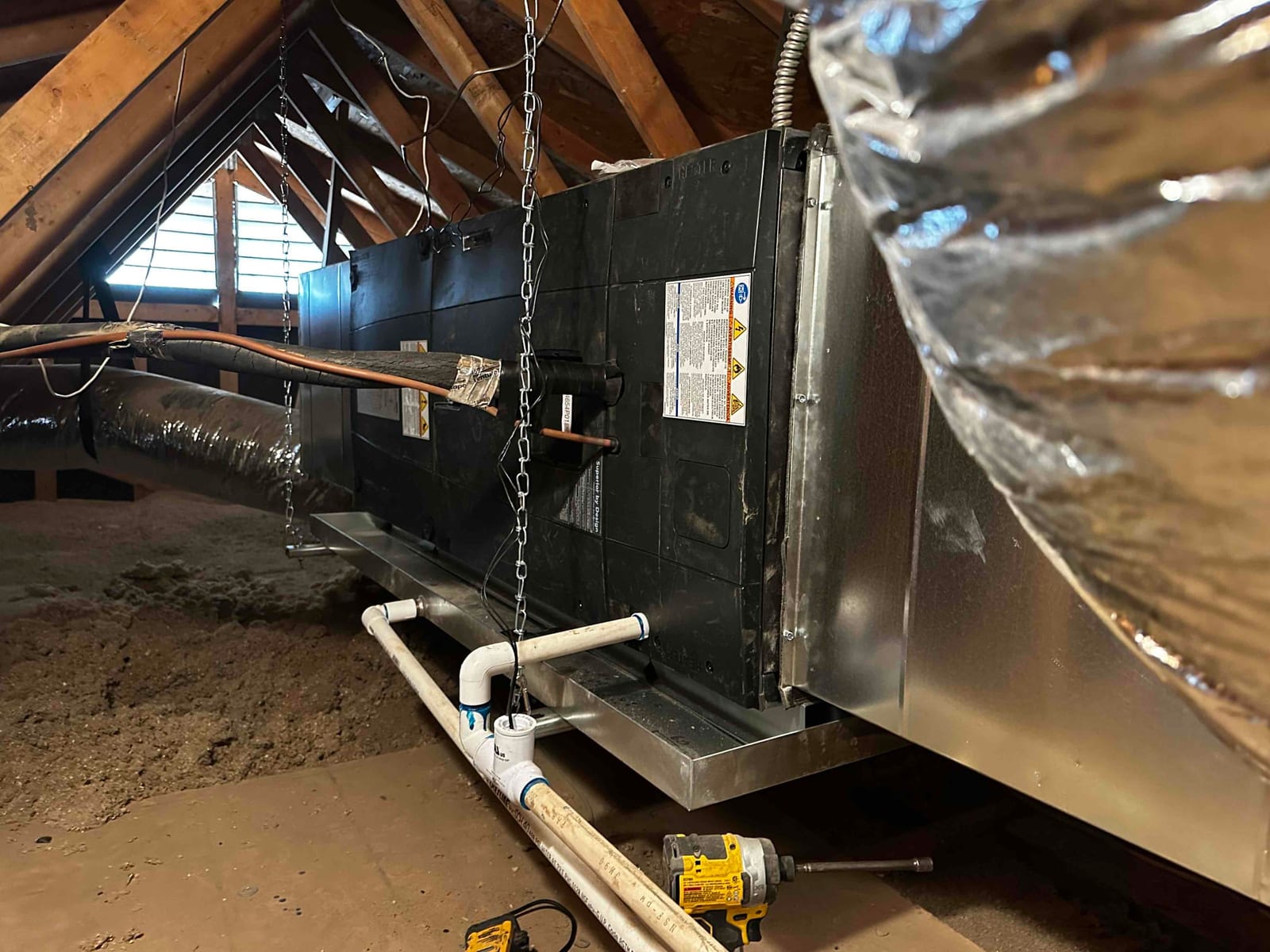 Air handler suspended in attic with insulated duct connections and new PVC condensate drain with cleanout and safety pan.
