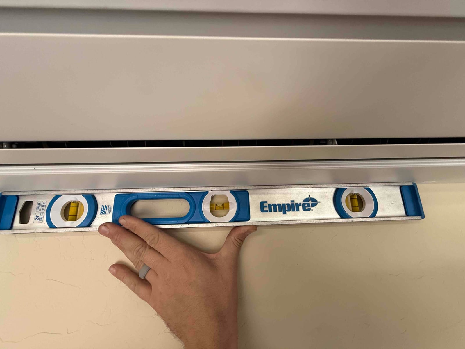 Installer checks the wall-mounted mini-split indoor unit for level using a spirit level along the bottom edge.