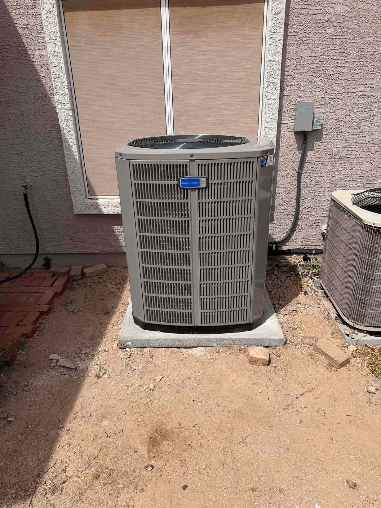 New outdoor heat pump condenser set on a level pad with electrical disconnect mounted on the wall beside it.
