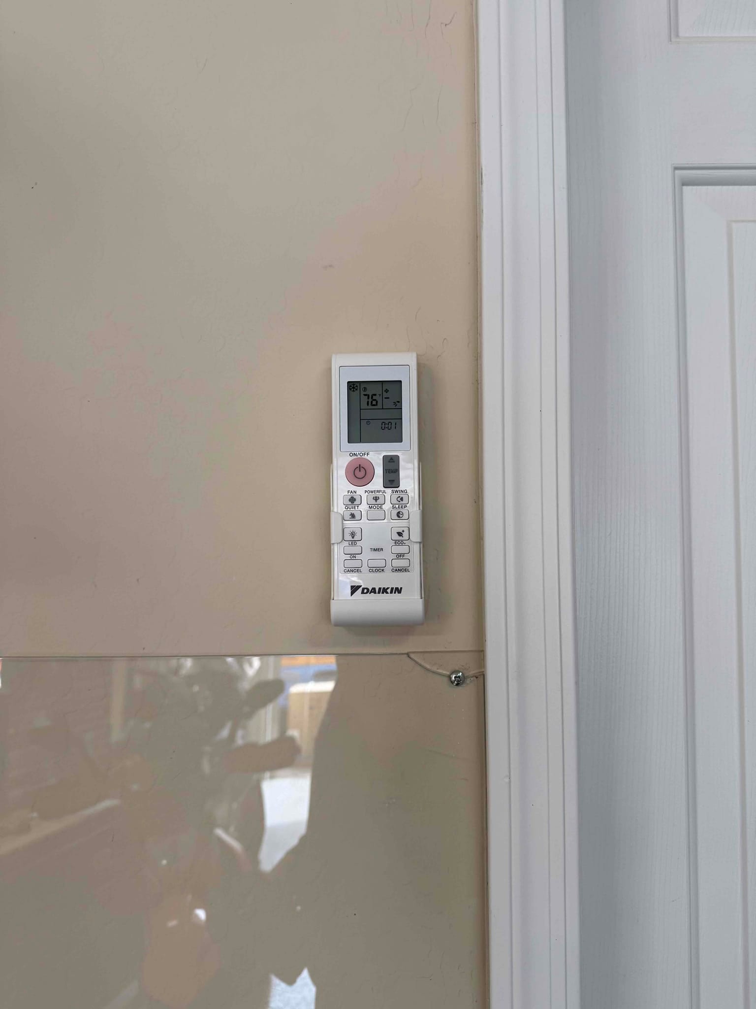 Wall-mounted mini-split remote control installed near a door, displaying a setpoint of 76 degrees Fahrenheit.