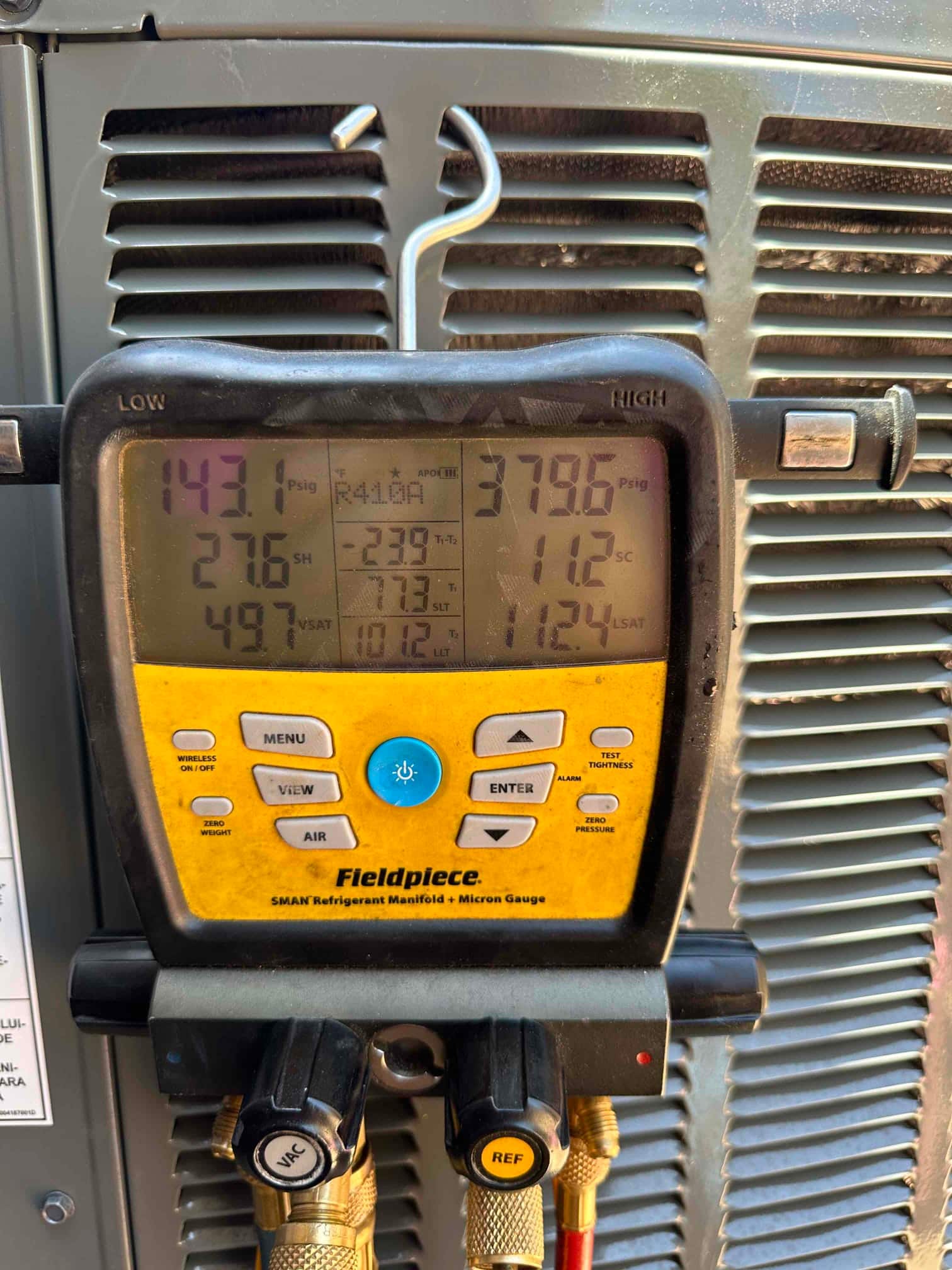Digital manifold connected to the outdoor unit shows 143 PSI suction and 379 PSI liquid while checking operating pressures.