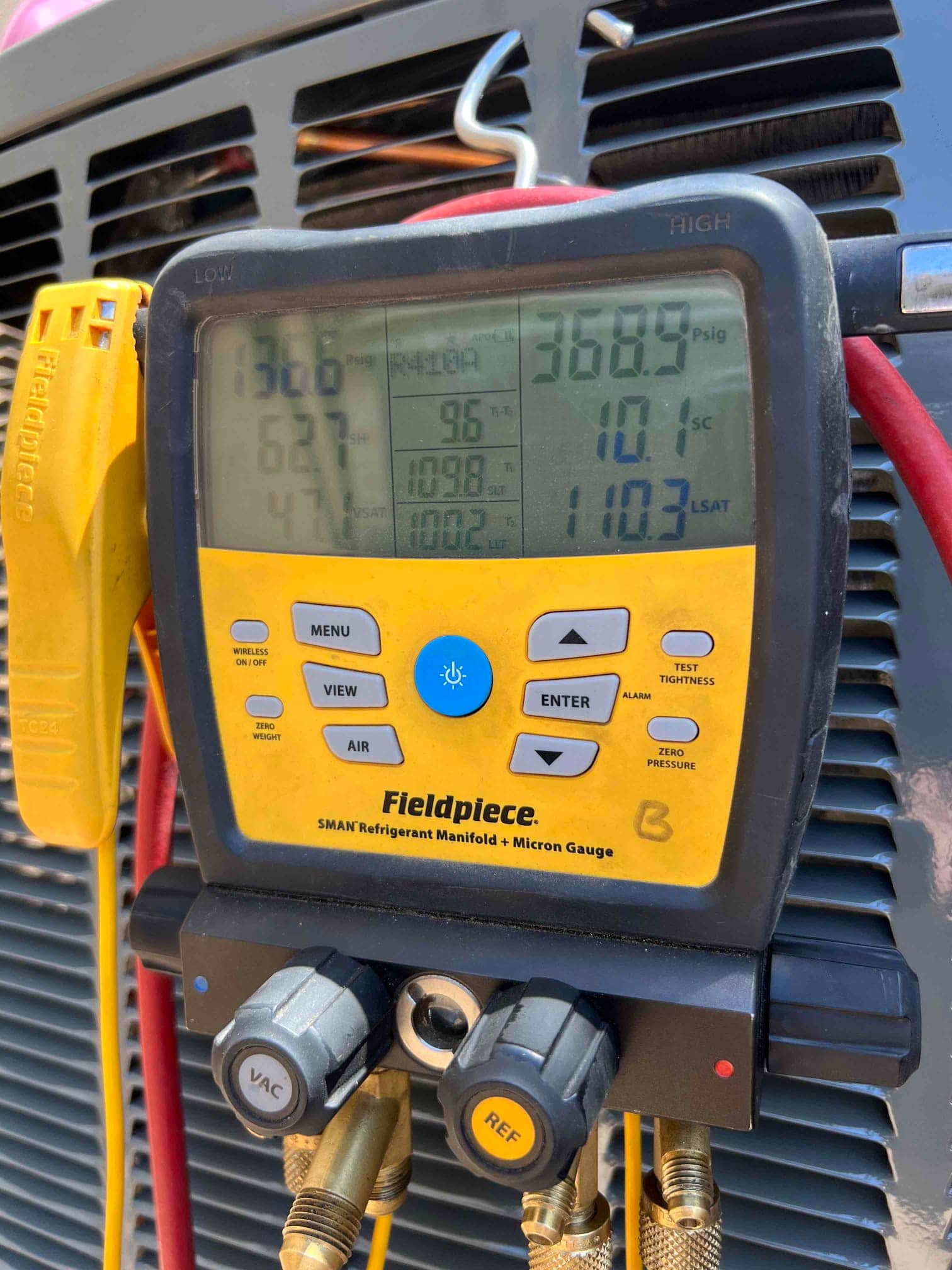 Digital manifold gauges on the outdoor unit show operating pressures and superheat/subcooling during system commissioning.