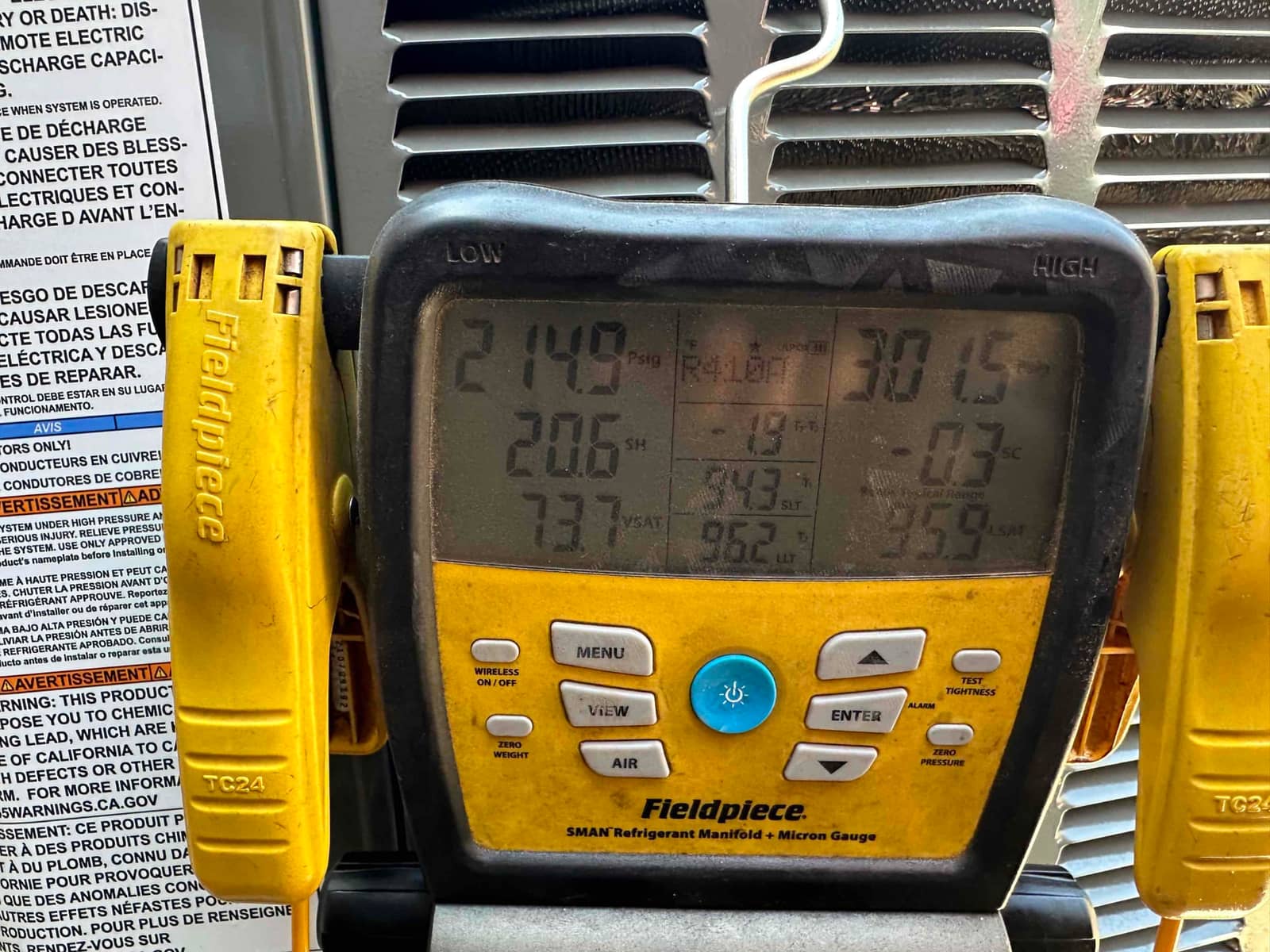 Digital manifold shows system operating with low side at 214 PSI and high side at 301 PSI during refrigerant commissioning.