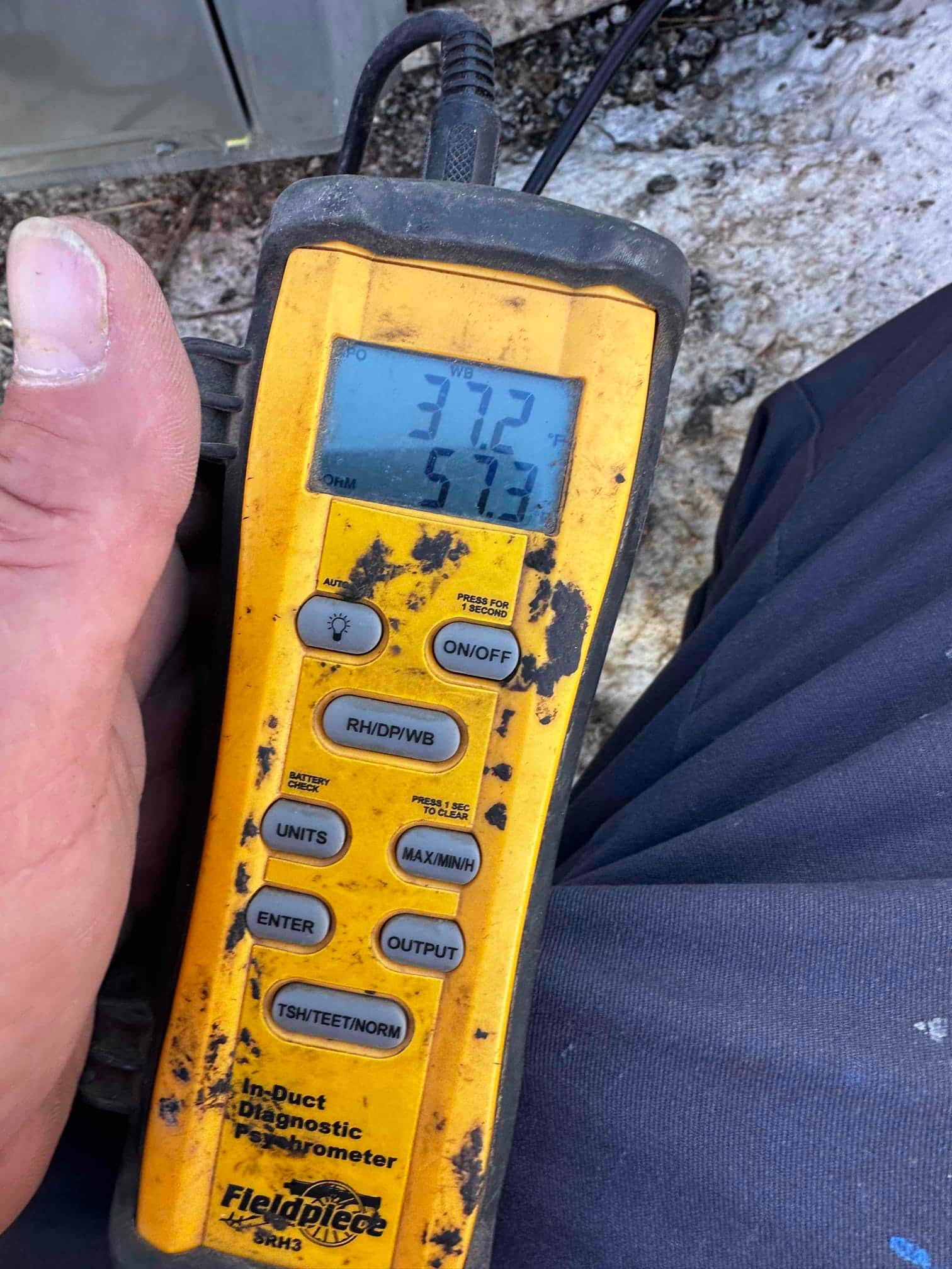 Digital psychrometer shows 57.3 degrees Fahrenheit, documenting cooled supply air temperature during system commissioning.