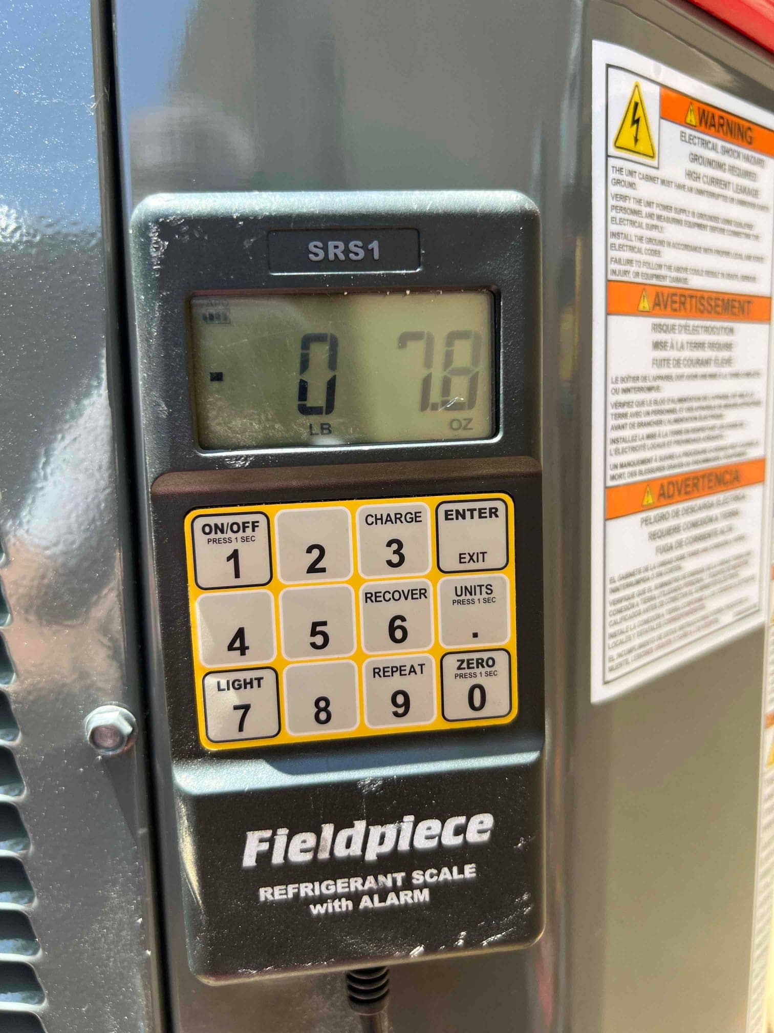 Digital refrigerant scale shows 0 pounds 7.8 ounces during charging at the outdoor condenser unit.