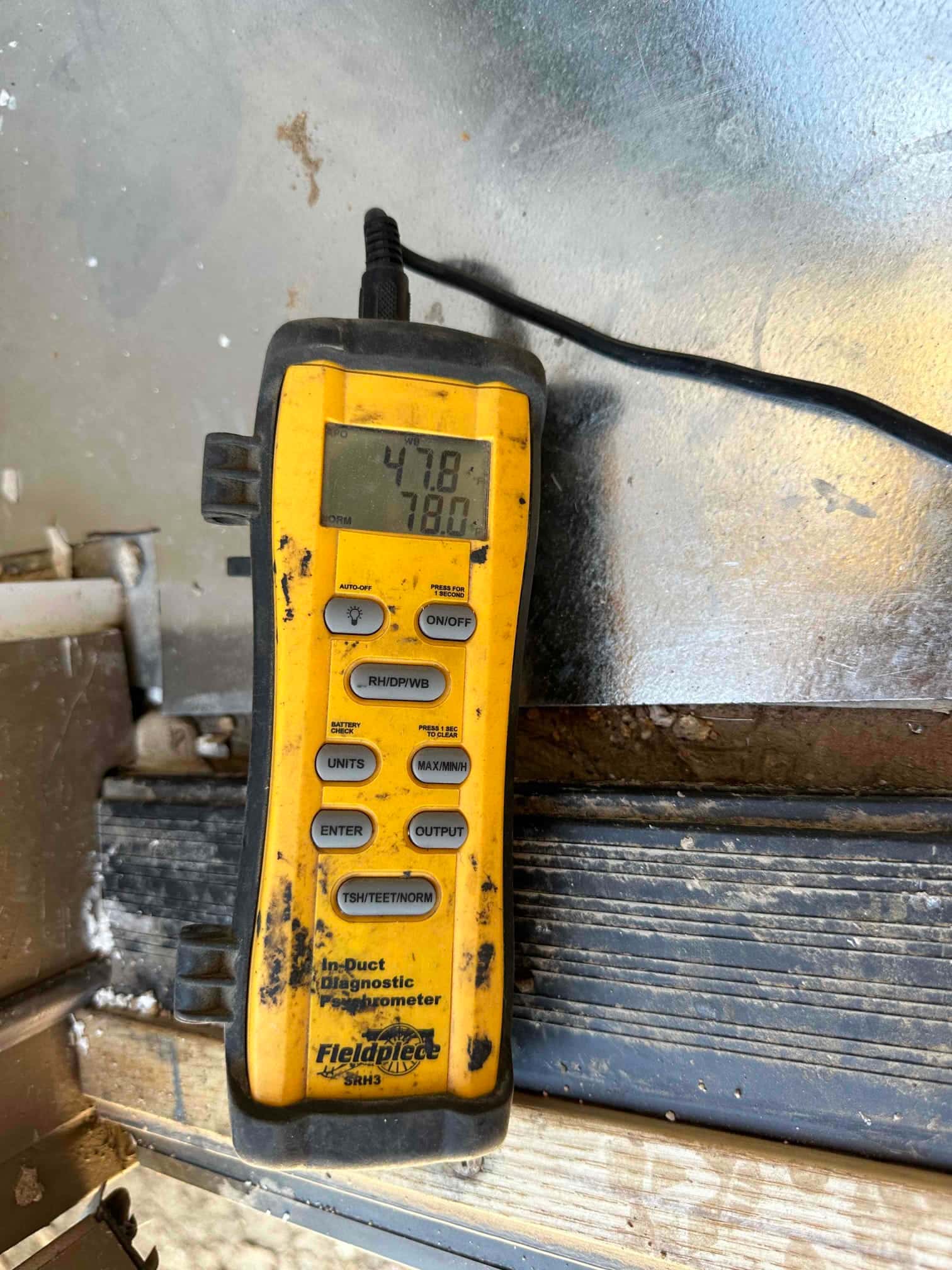 Digital thermometer displays 47.8°F and 78.0°F while measuring air temperatures during system commissioning at the duct.