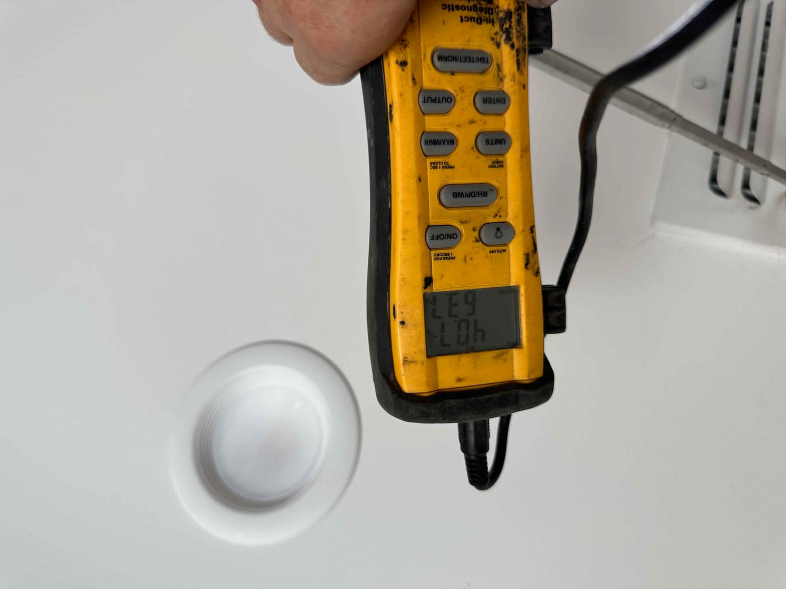 Digital thermometer held at a ceiling supply register displays 63 degrees, documenting cooled air temperature leaving the evaporator.